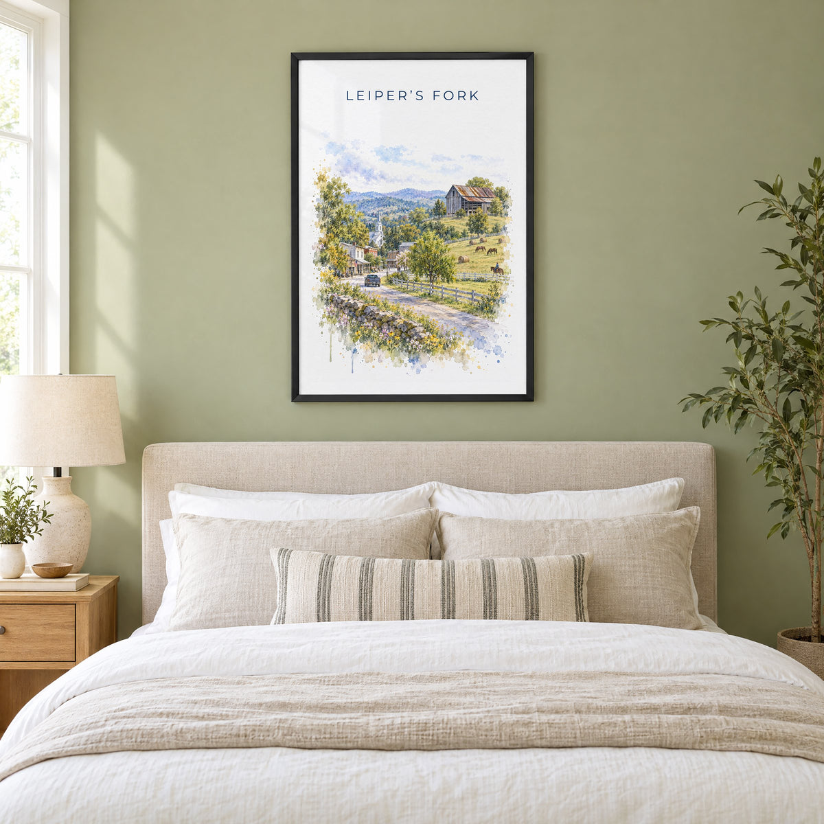 Leiper's Fork, Tennessee watercolor print in a black frame above an upholstered headboard in a sage green bedroom