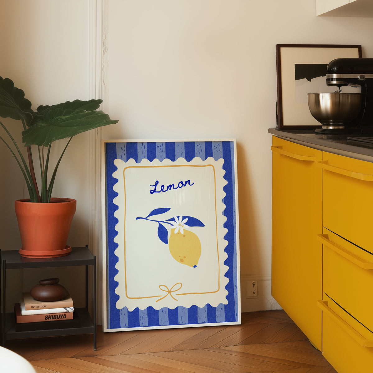 Lemon branch print in a white frame leaning on parquet beside a bright yellow kitchen
