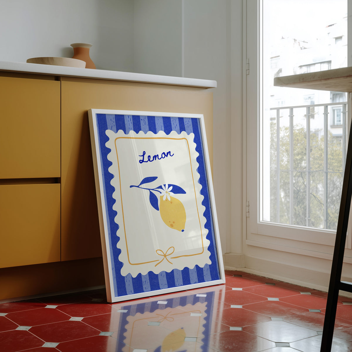 Lemon branch print in a white frame against yellow cabinets on a red tiled floor