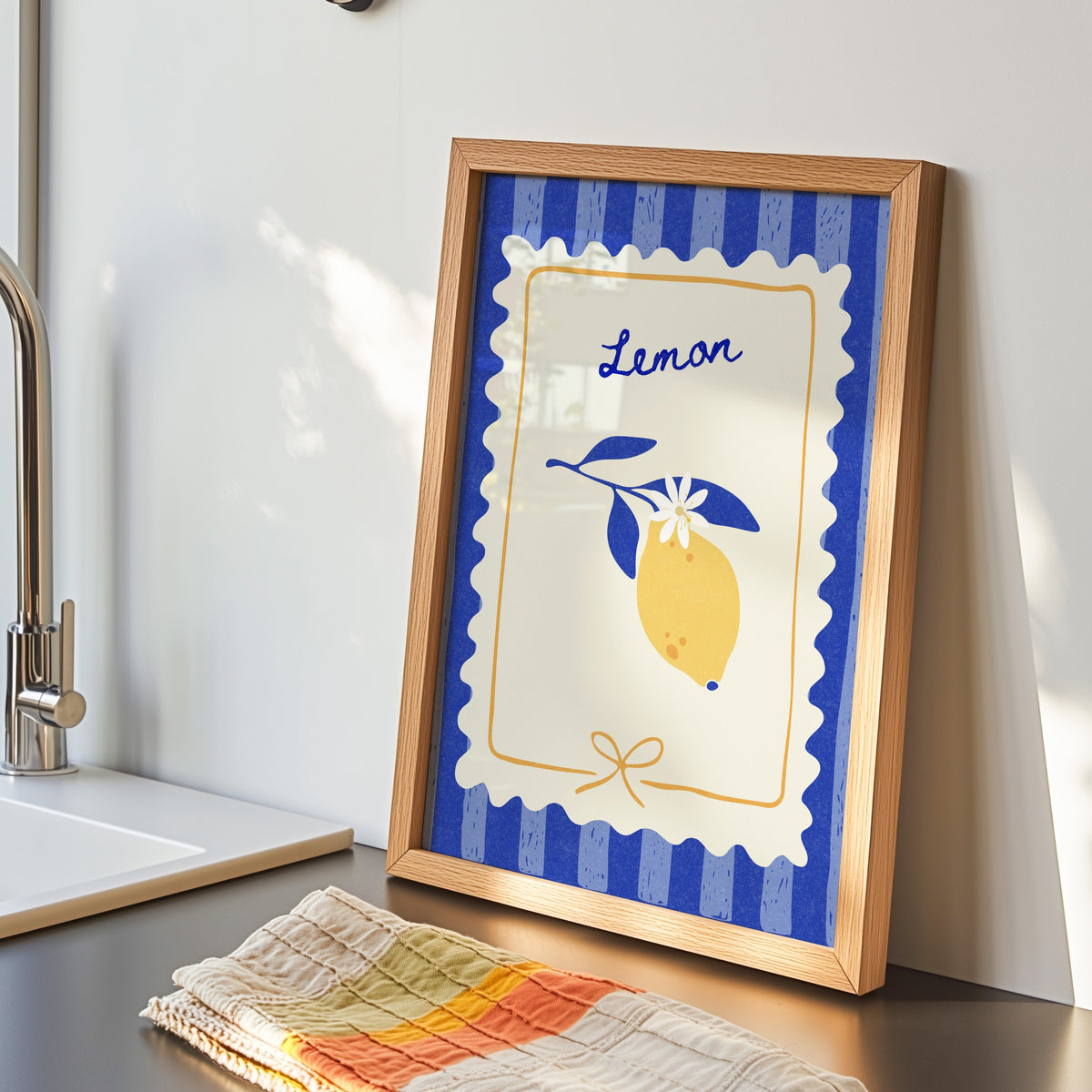 Lemon branch print in an oak frame by the kitchen sink beside a striped tea towel