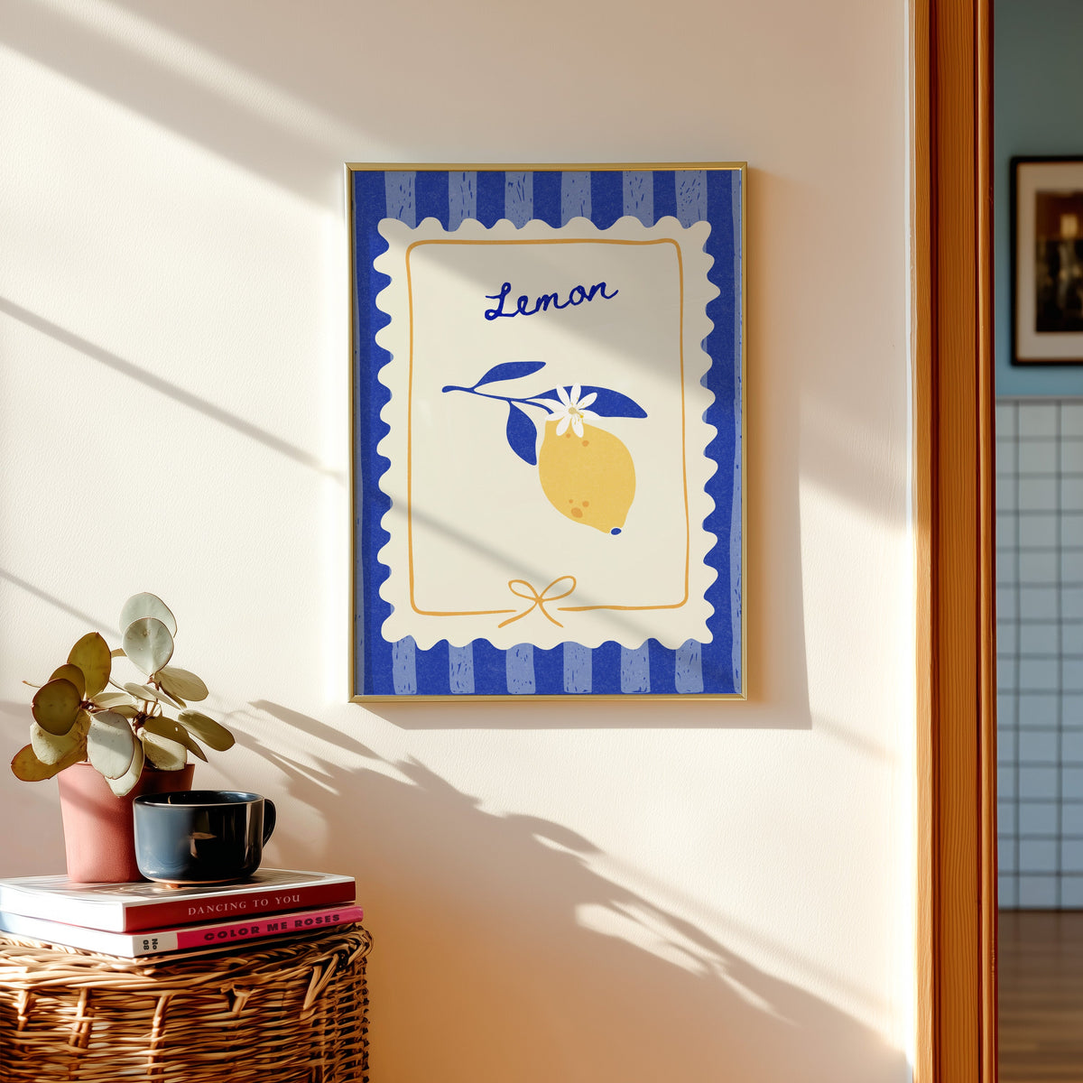 Lemon branch print in a gold frame above a basket of books and a pilea plant