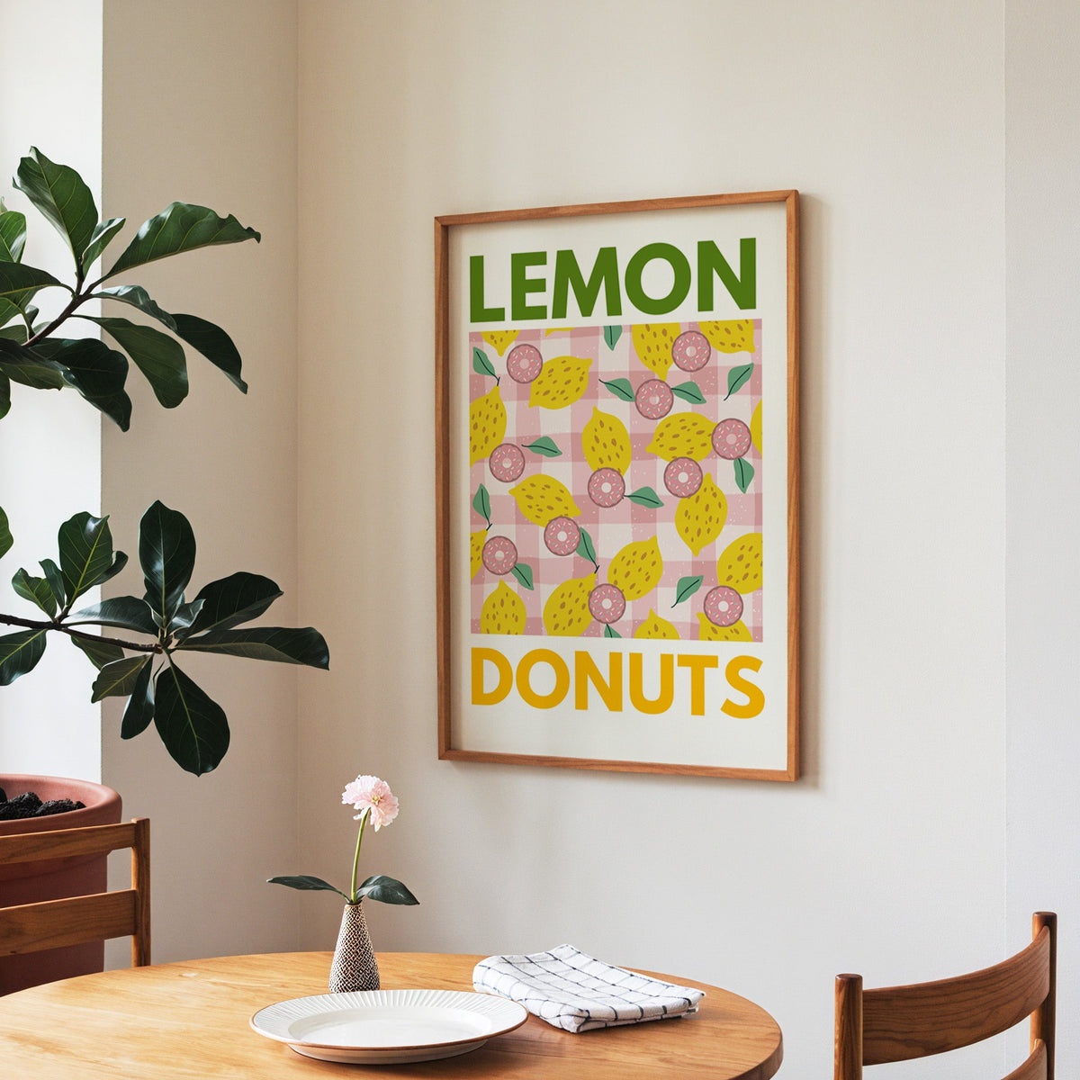 Lemon and donuts print in a walnut frame above a round table beside a fiddle-leaf fig
