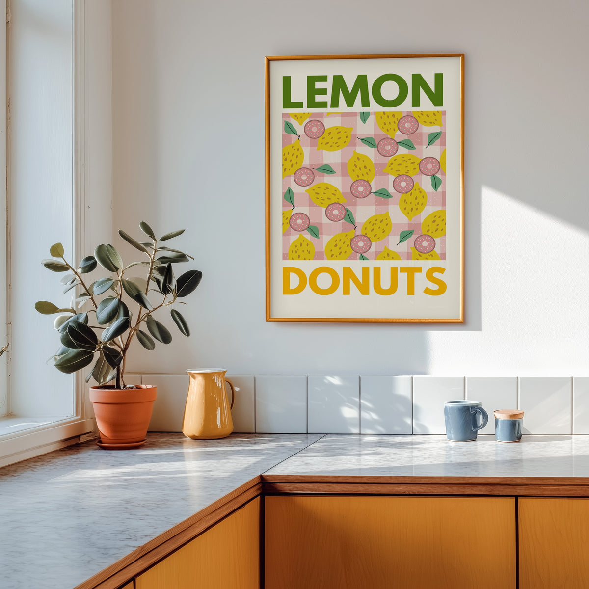 Lemon and donuts print shown in a gold frame above a marble counter in a tan kitchen
