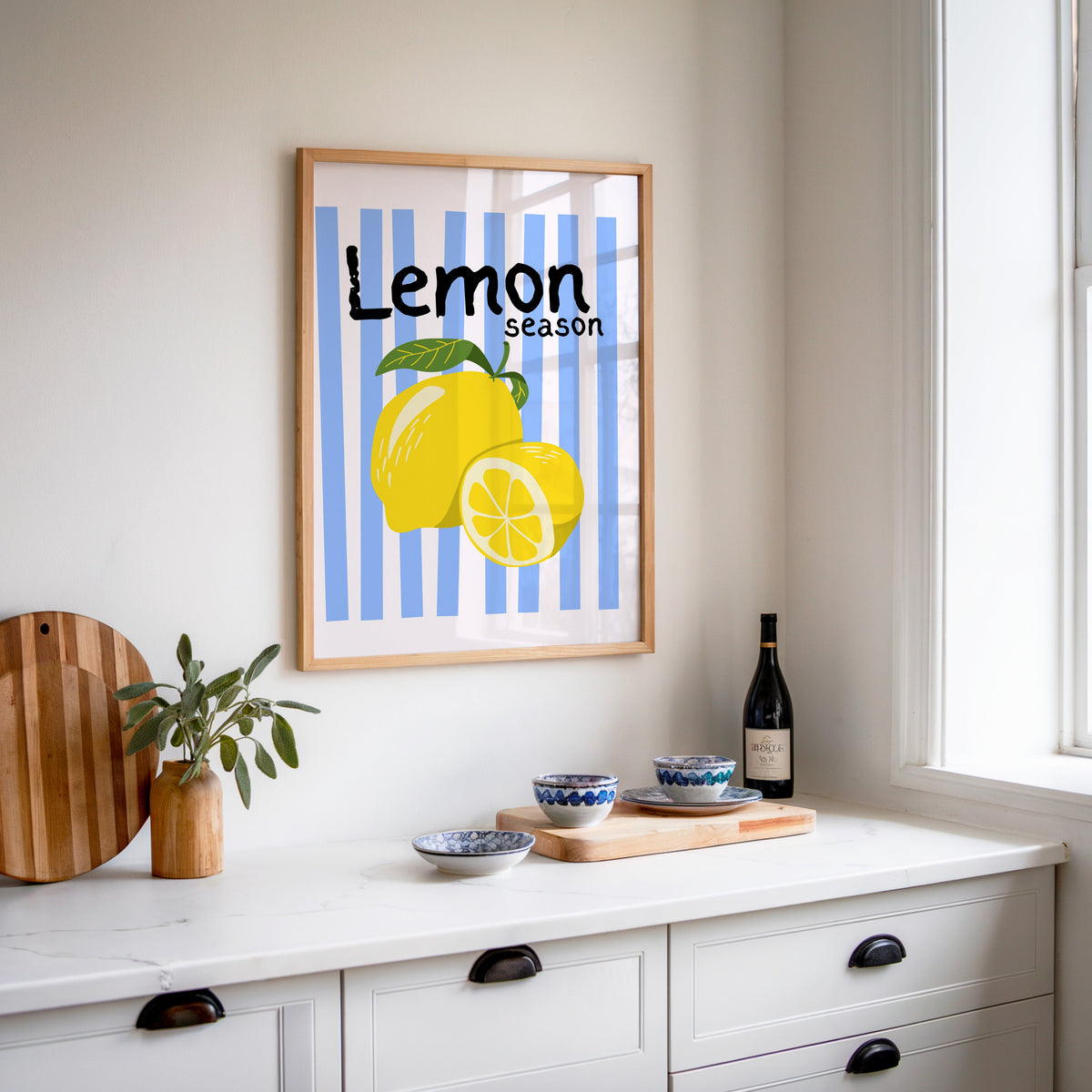 Lemon Season print in an oak frame above a white sideboard with a bottle of wine