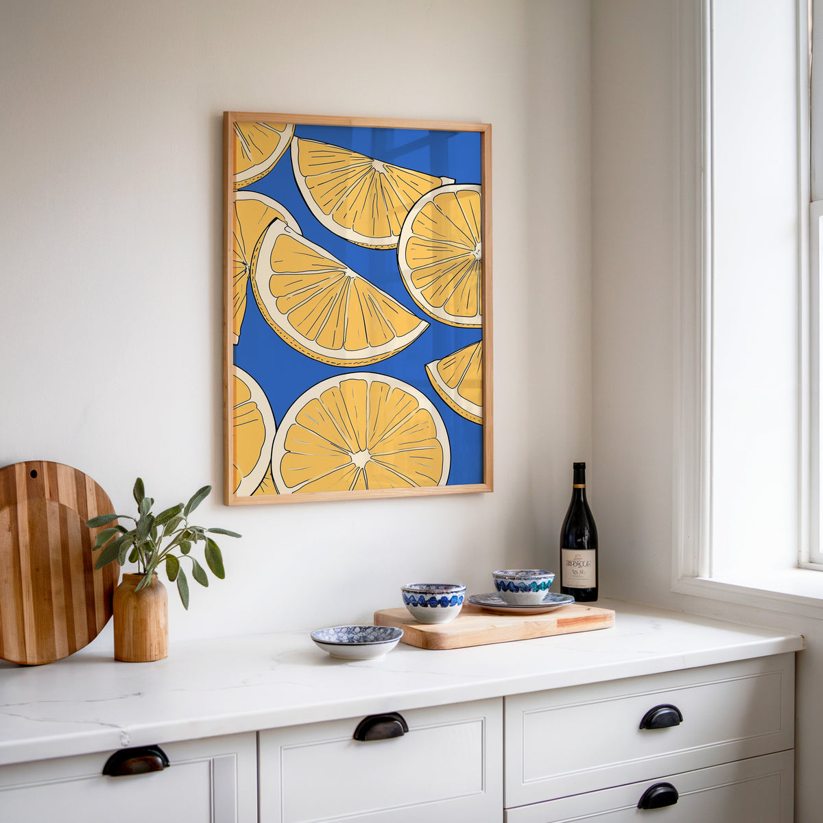 Lemon slice pattern print in an oak frame above a white sideboard with a bottle of wine