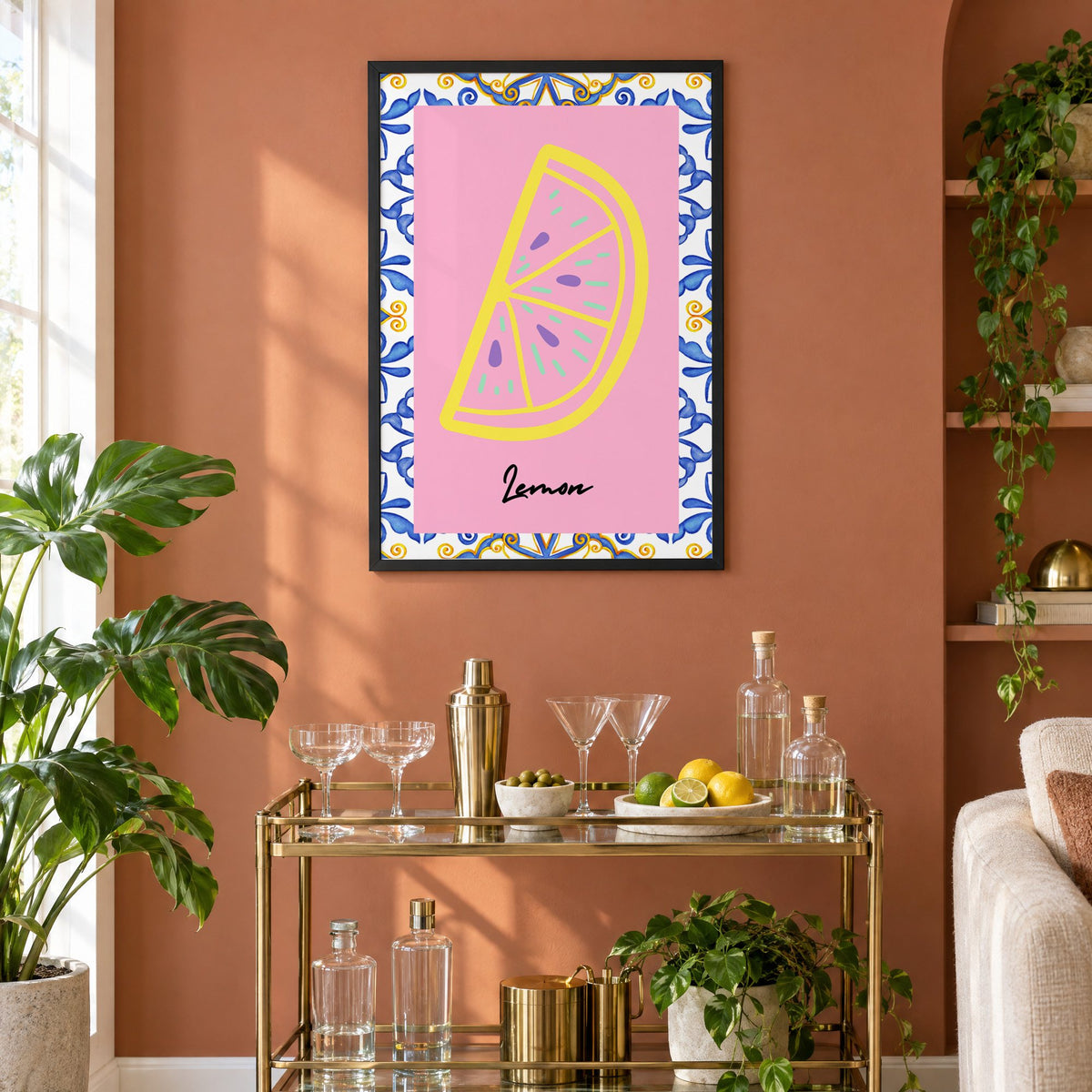 Lemon slice pink majolica tile print in a black frame on a terracotta wall above a brass bar cart with coupes and citrus