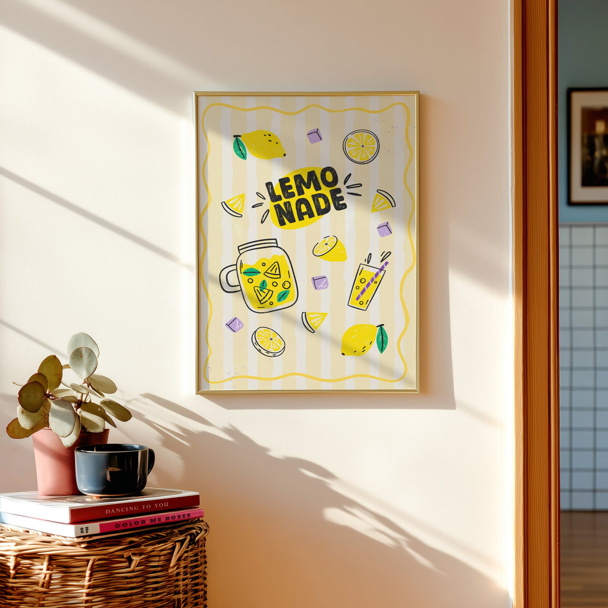 Lemonade print in a gold frame above a basket of books and a pilea plant