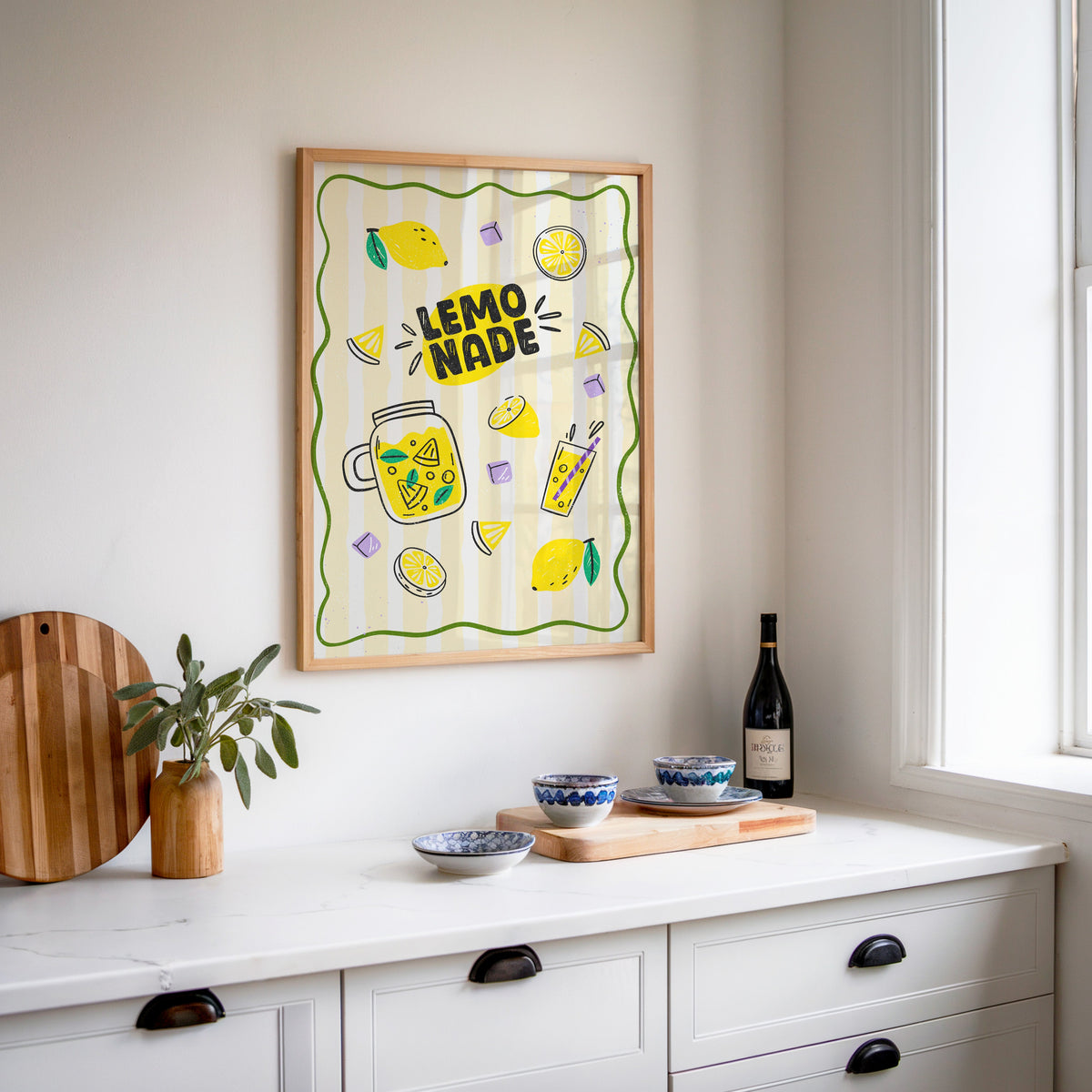 Lemonade Stand print in an oak frame above a white sideboard with a bottle of wine