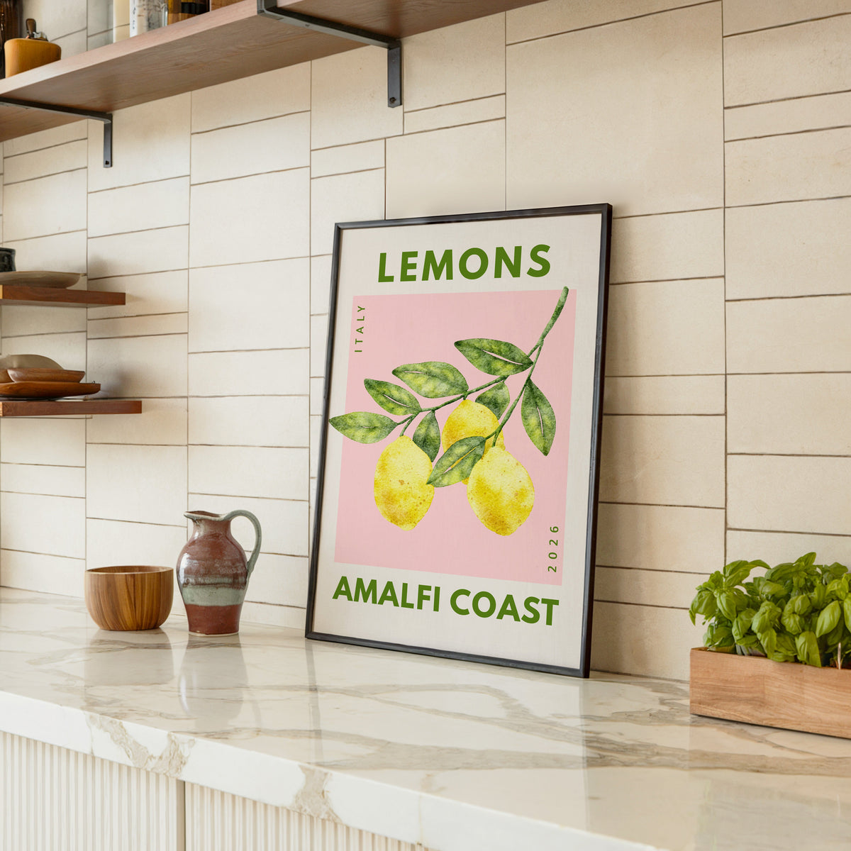 Lemons Amalfi Coast print in a black frame leaning on a marble counter in a tiled kitchen