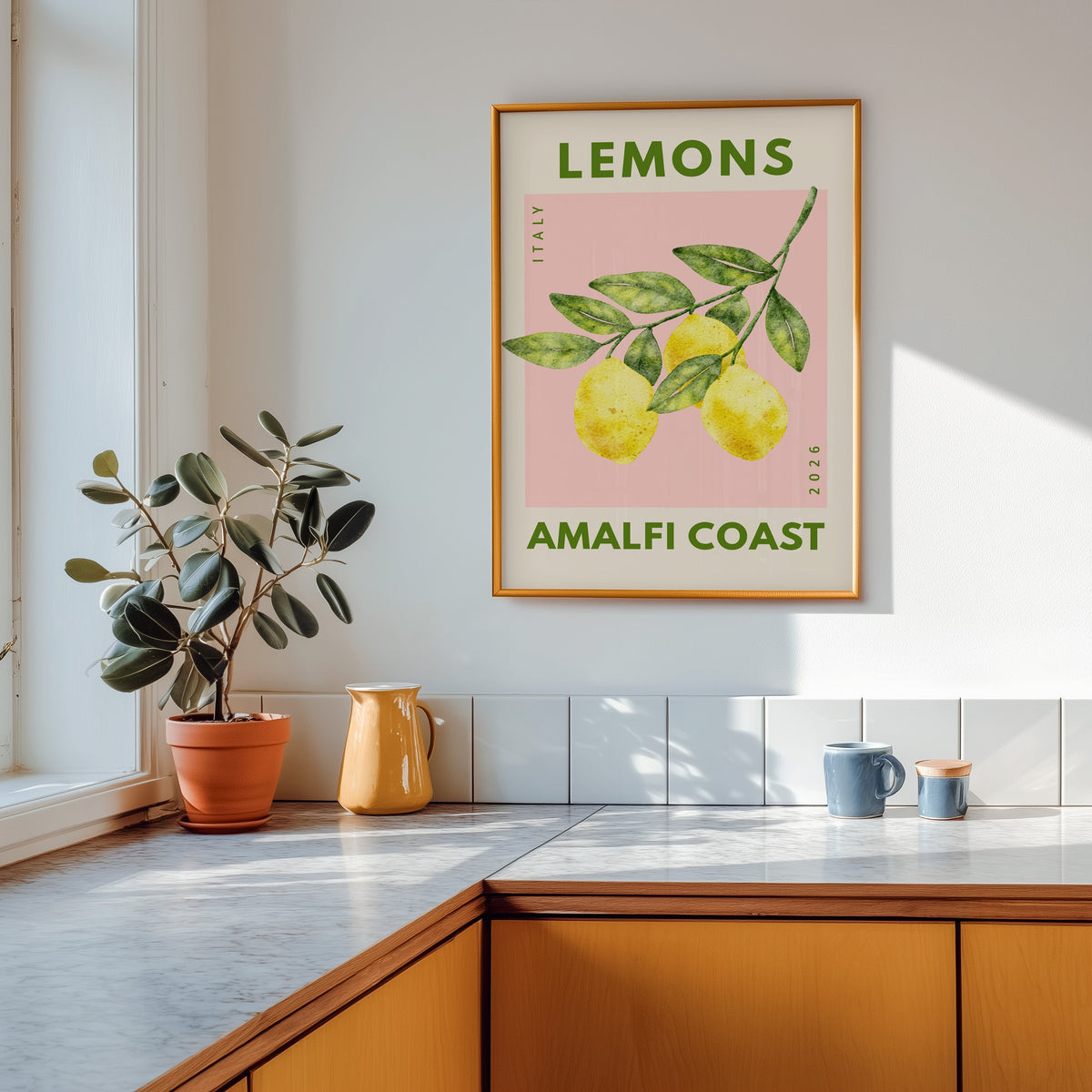 Lemons Amalfi Coast print shown in a gold frame above a marble counter in a tan kitchen