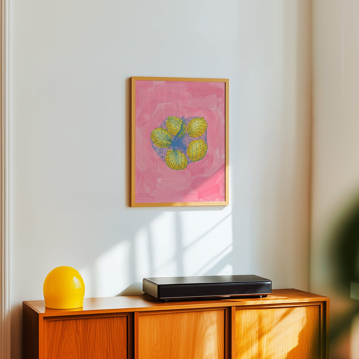 Market lemons print in a light oak frame above a teak sideboard with a yellow lamp