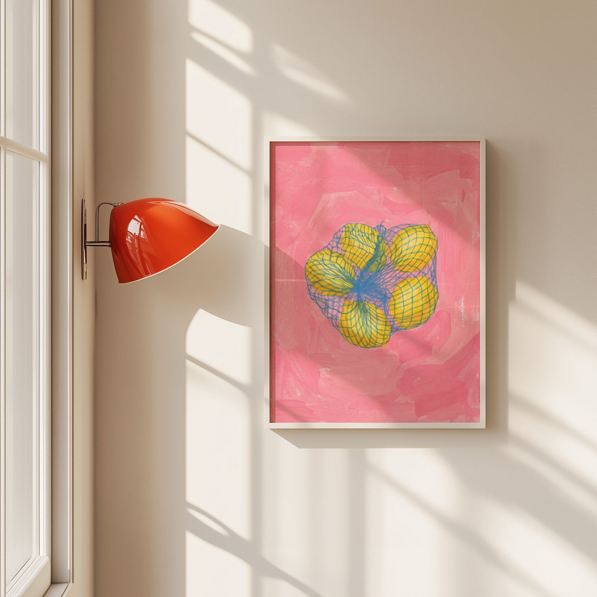 Lemons in mesh bag print in a white frame beside a red wall sconce