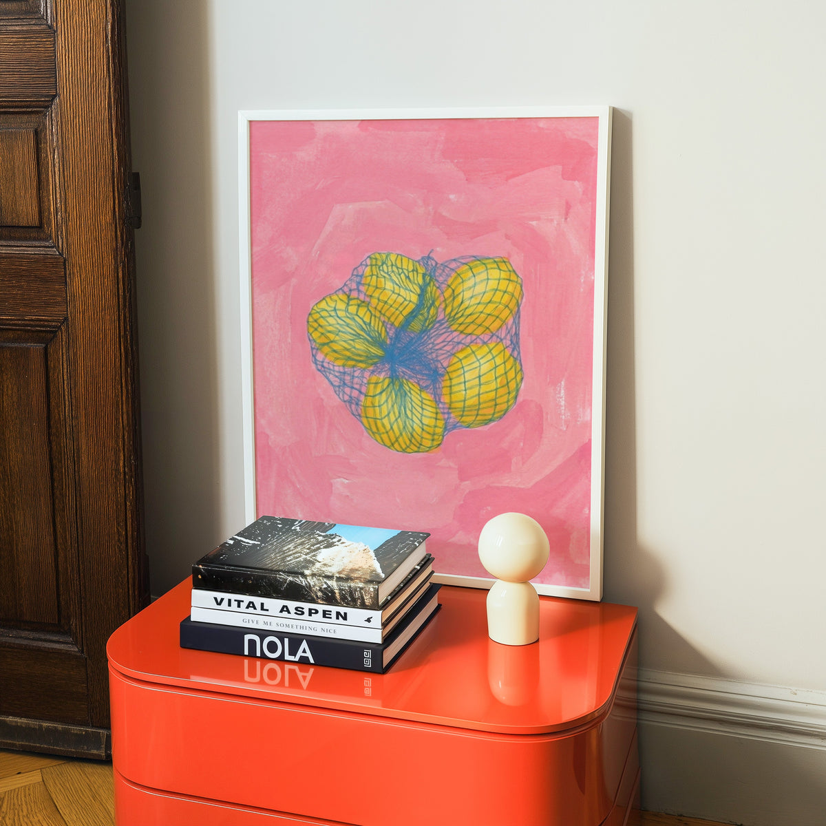 Citrus kitchen print in a white frame on a glossy orange cabinet with books