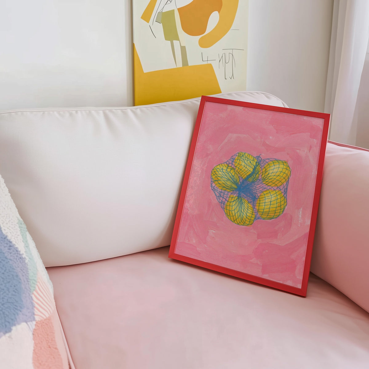 Lemon still life print shown in a red frame leaning on a blush pink sofa