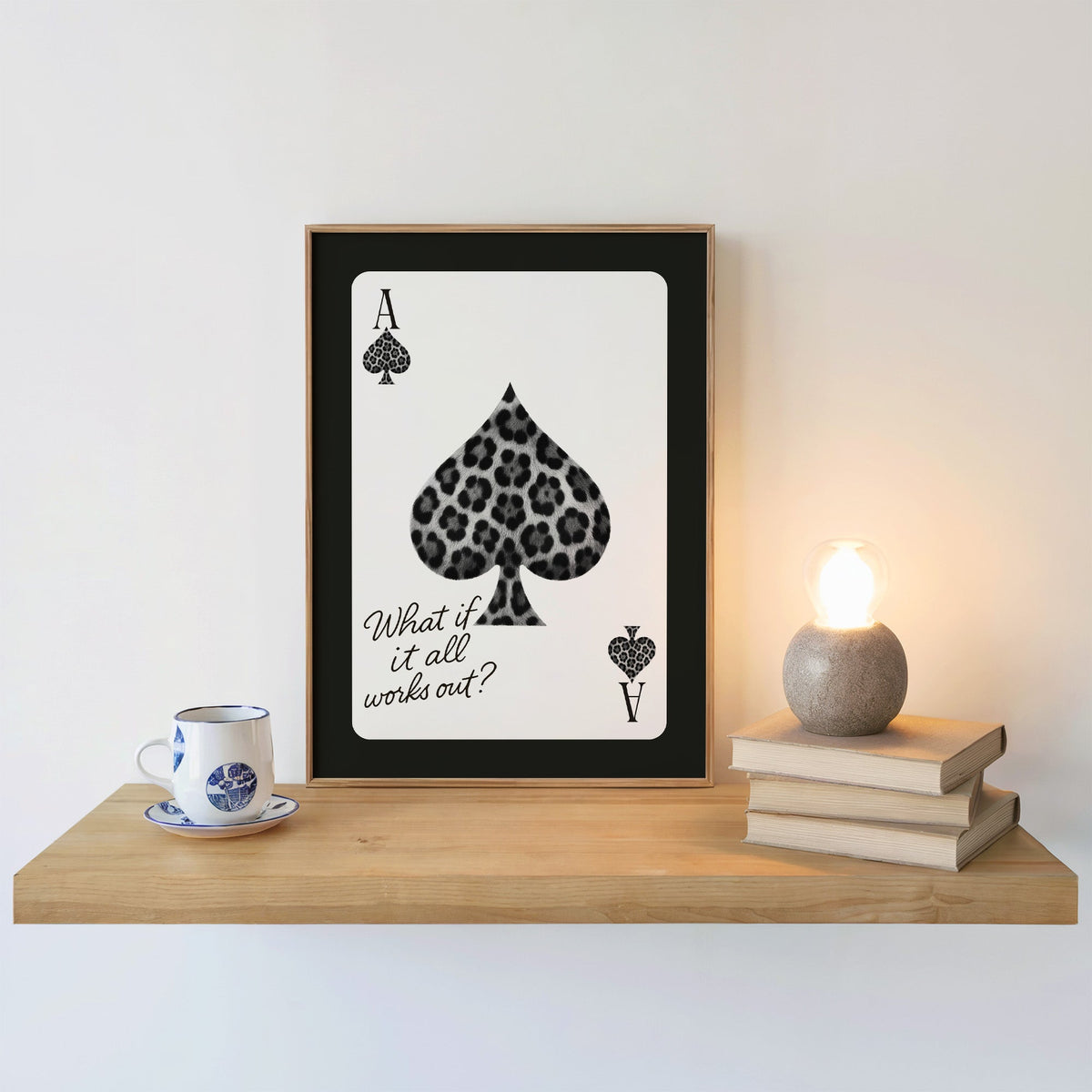 Leopard fur ace of spades card print in an oak frame on a floating shelf beside a glowing lamp