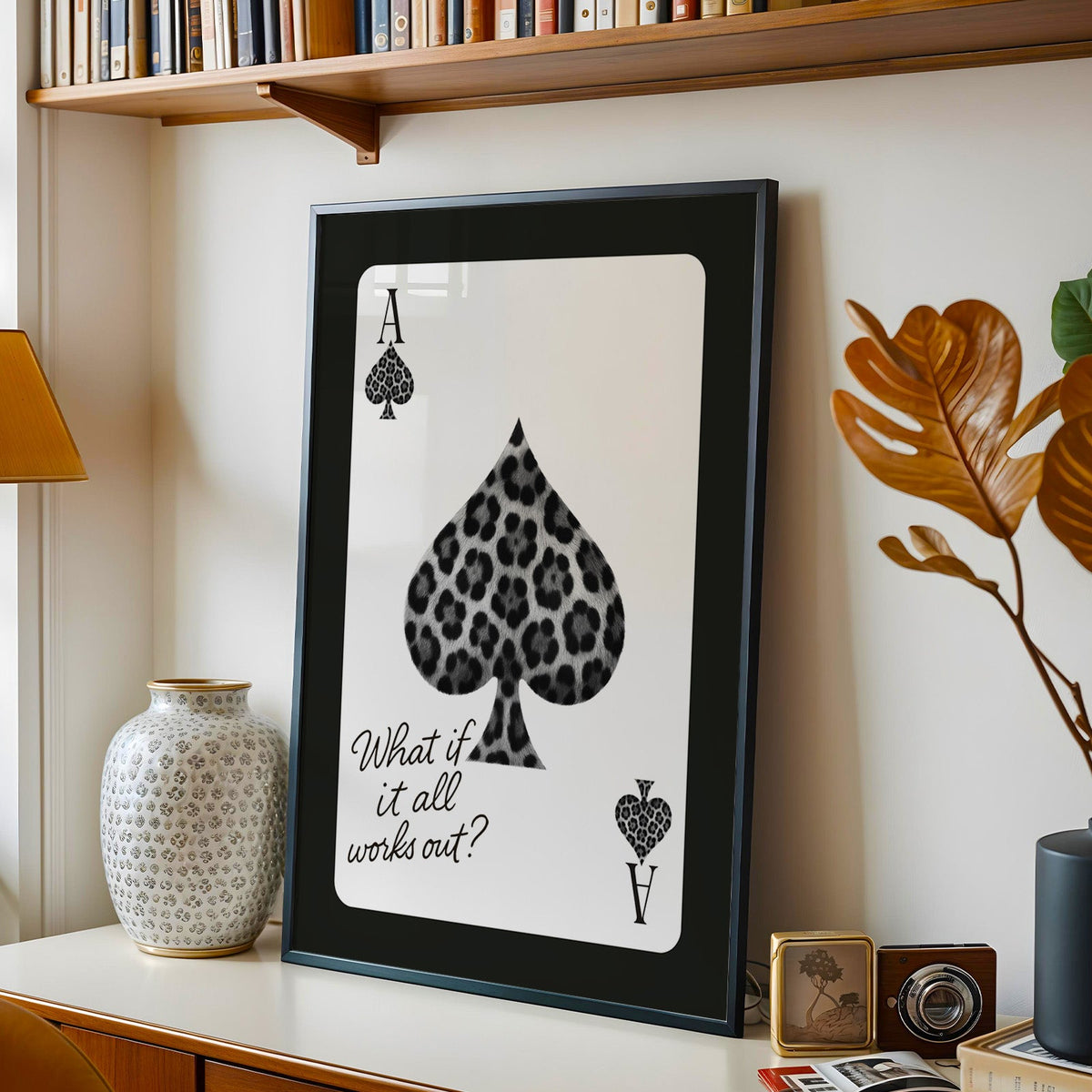 Leopard fur ace of spades card print in a black frame on a console under a bookshelf