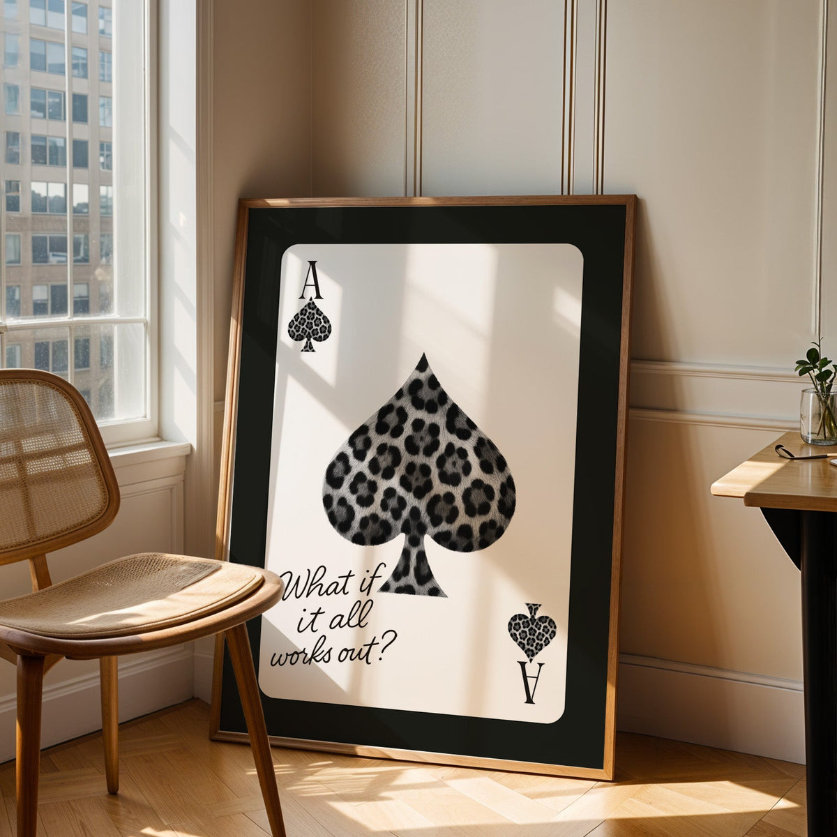 Leopard fur ace of spades card print in an oak frame leaning in a sunlit corner beside a cane chair