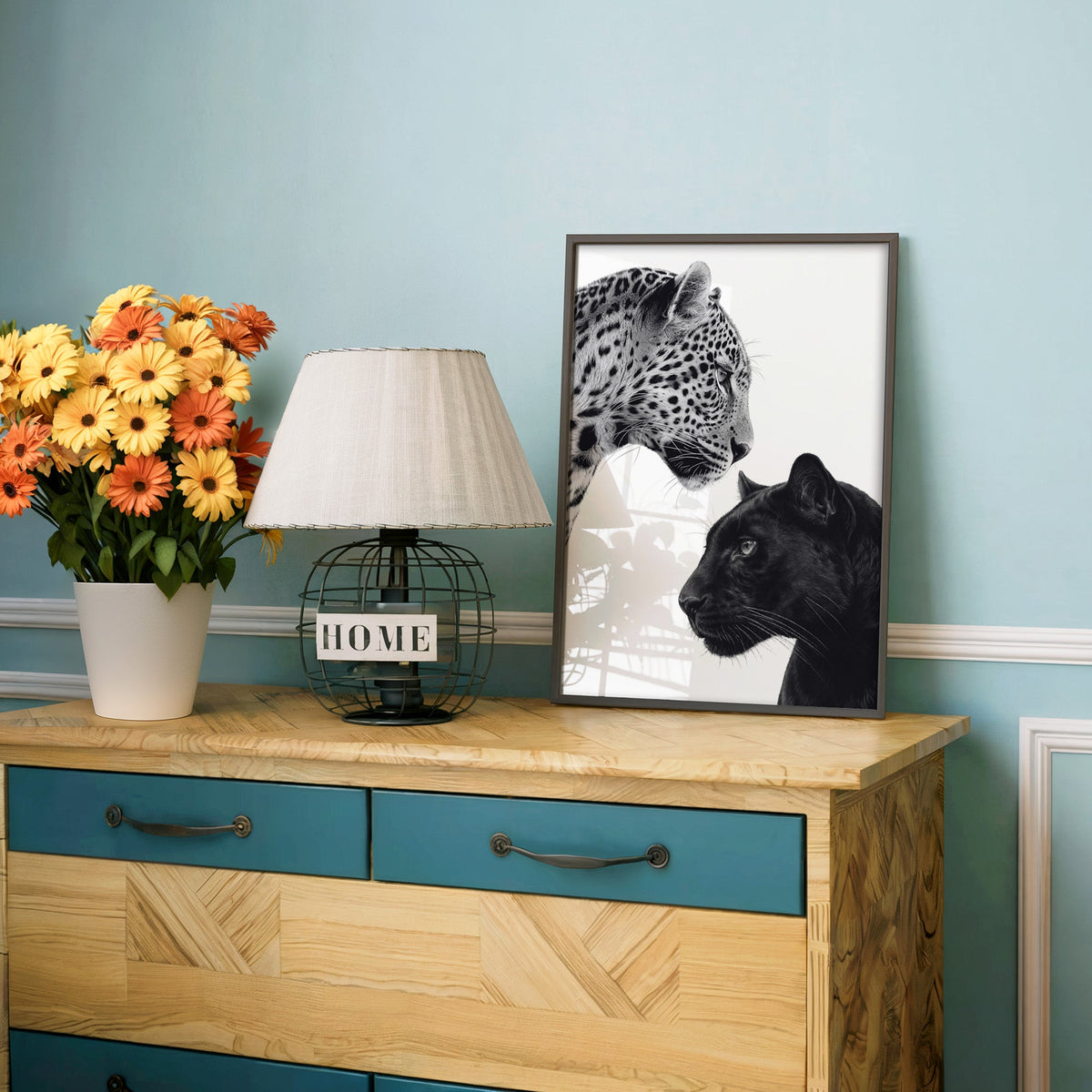Leopard and black panther facing each other print in a charcoal frame on a teal dresser beside orange daisies