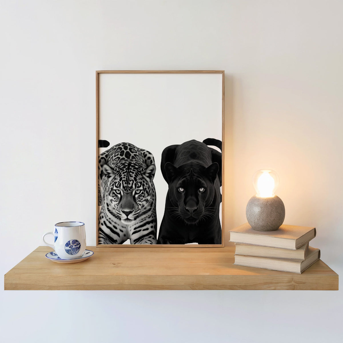 Spotted leopard and black panther facing forward print in an oak frame on a floating shelf beside a glowing lamp