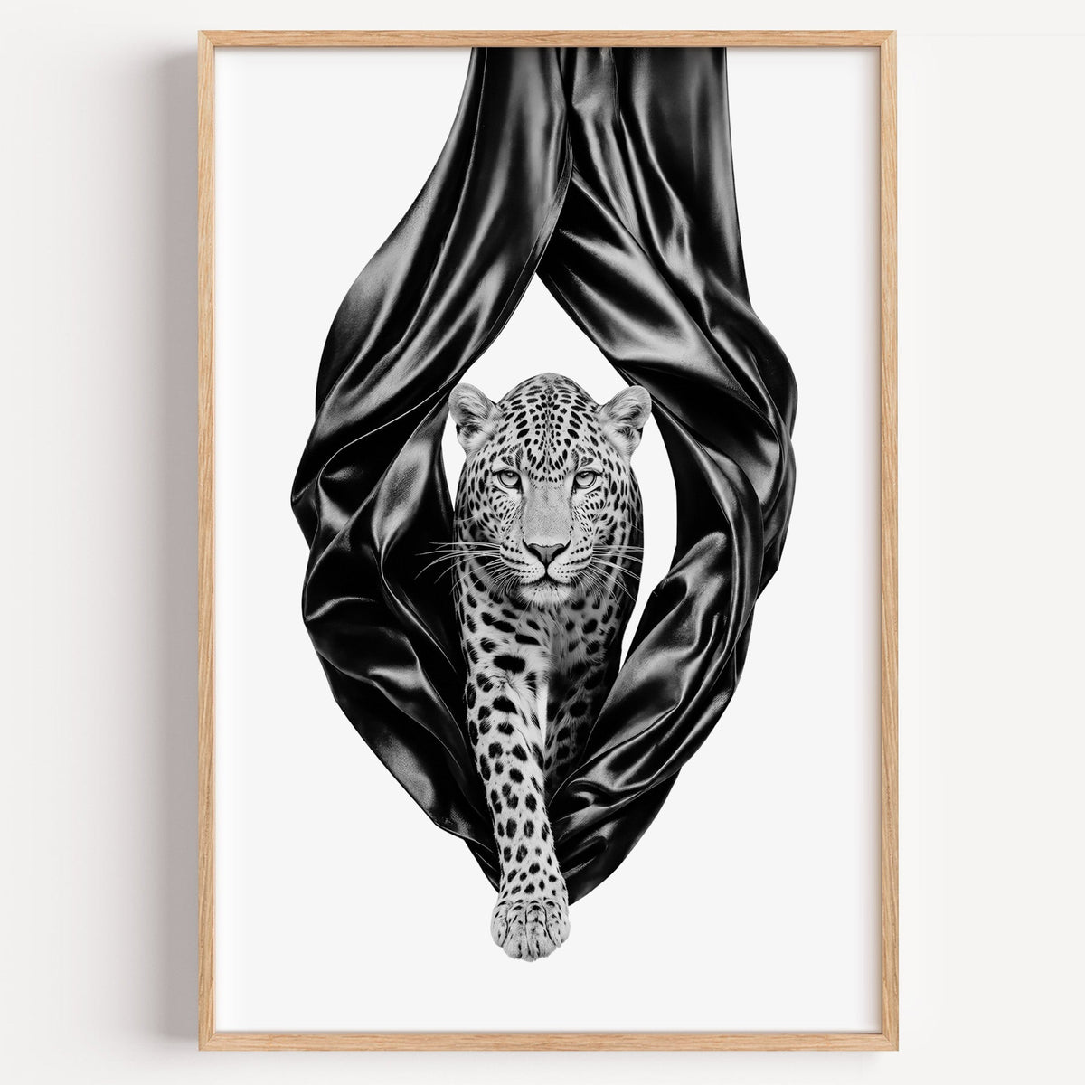 Leopard stepping out of black satin drapes print in a light oak frame on a plain white wall
