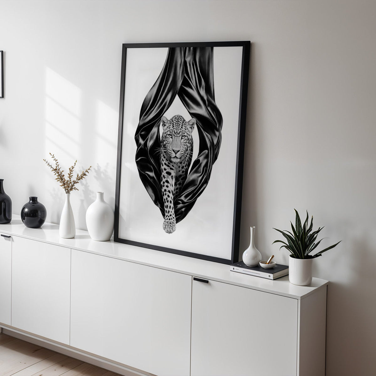 Leopard stepping out of black satin drapes print in a black frame on a white sideboard with black and white vases