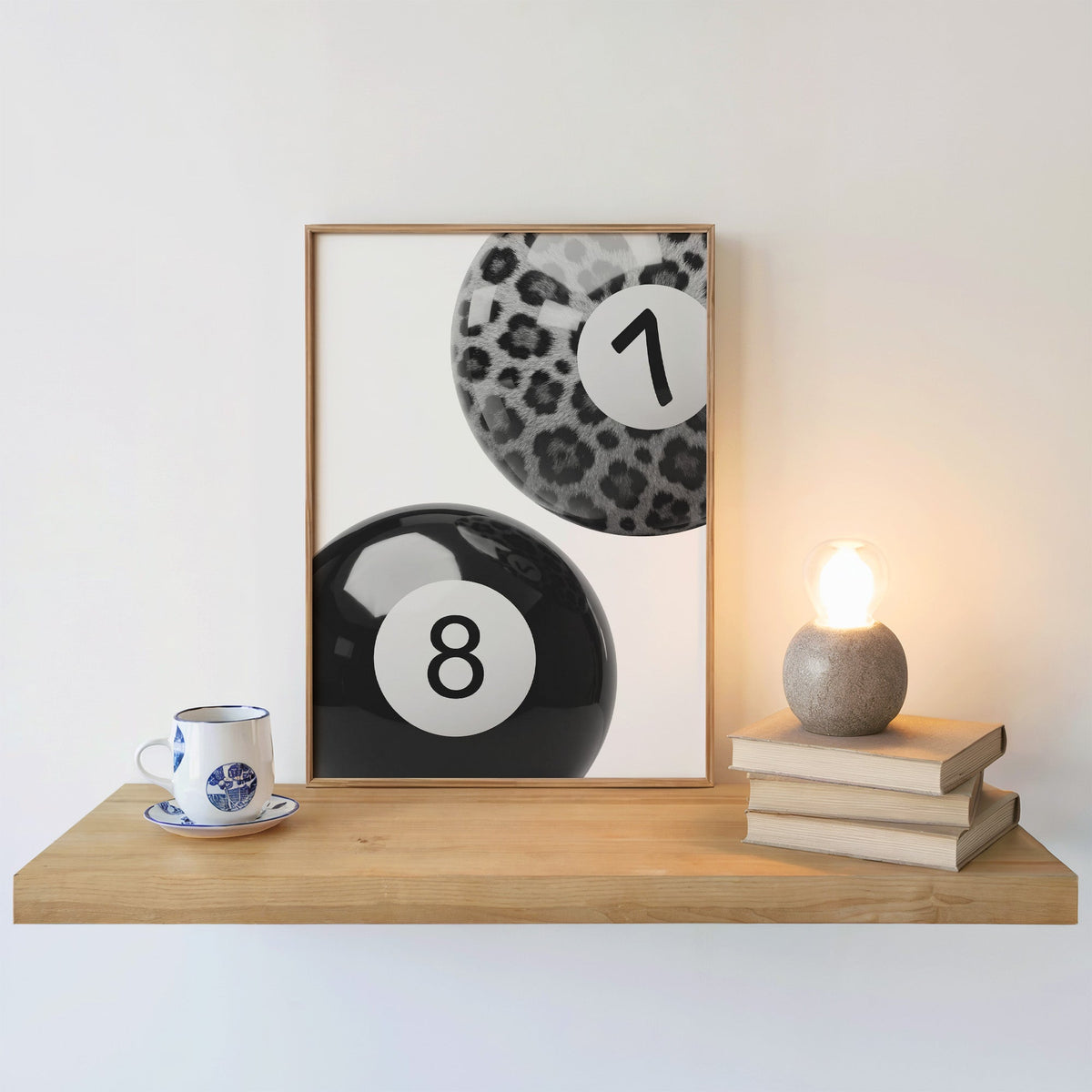 Leopard fur seven ball and black eight ball print in an oak frame on a floating shelf beside a glowing lamp