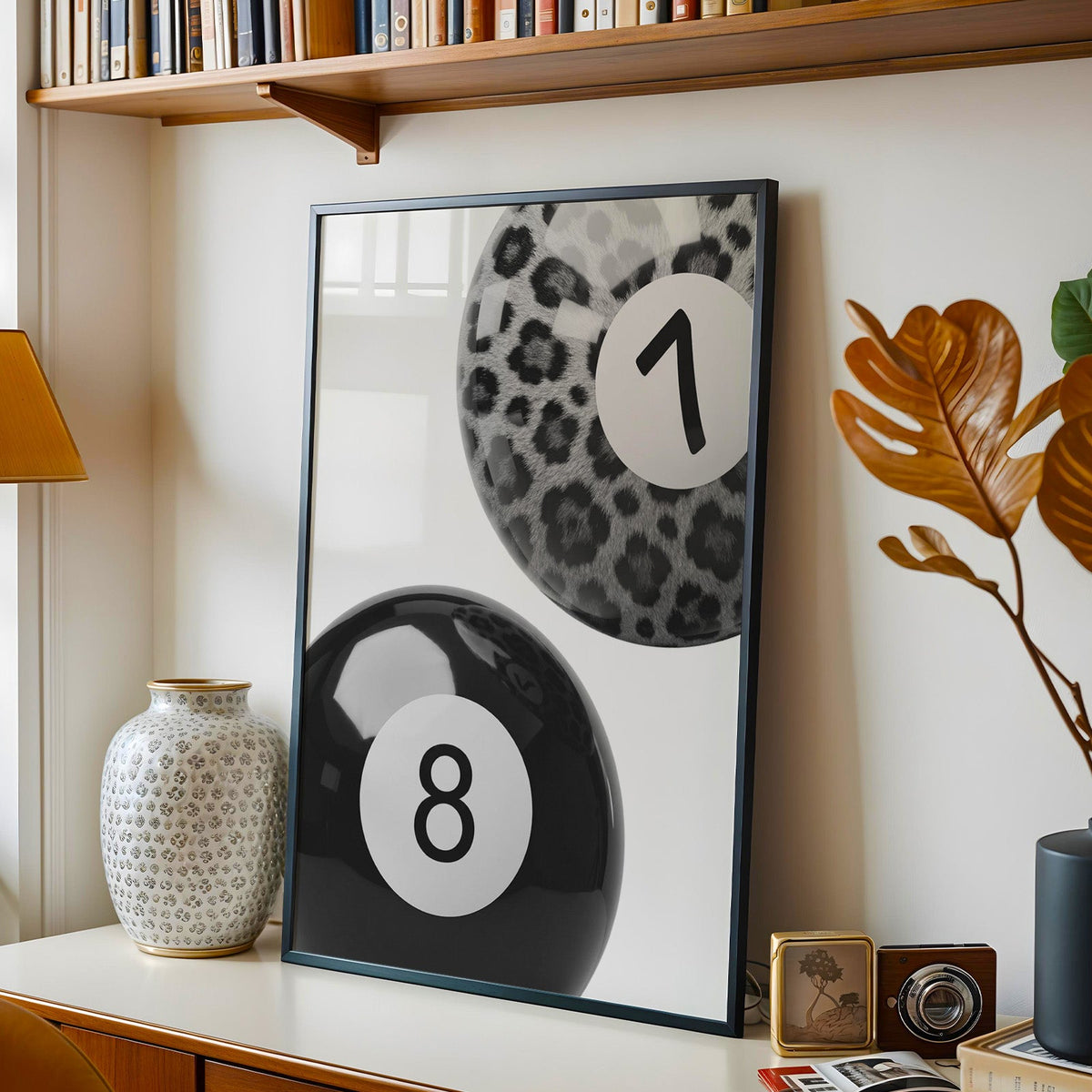 Leopard fur seven ball and black eight ball print in a black frame on a console under a bookshelf
