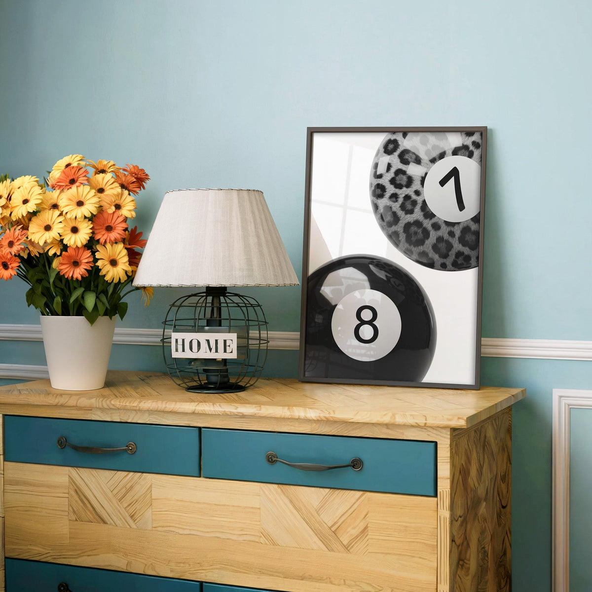 Leopard fur seven ball and black eight ball print in a charcoal frame on a teal dresser beside orange daisies