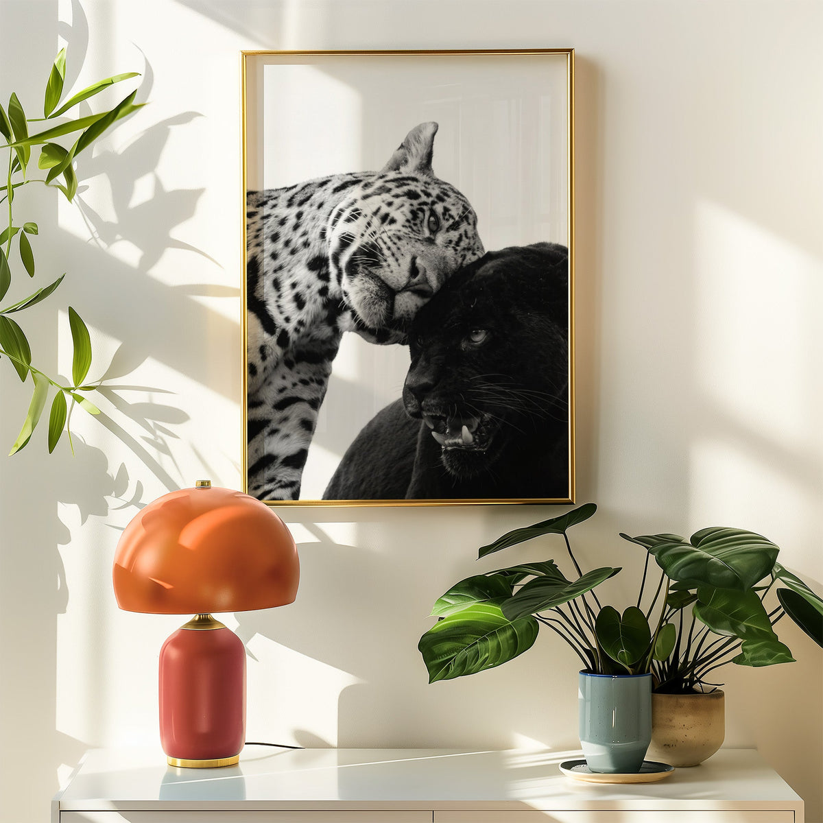 Leopard nuzzling black panther close-up print shown in a gold frame above a white sideboard with an orange lamp
