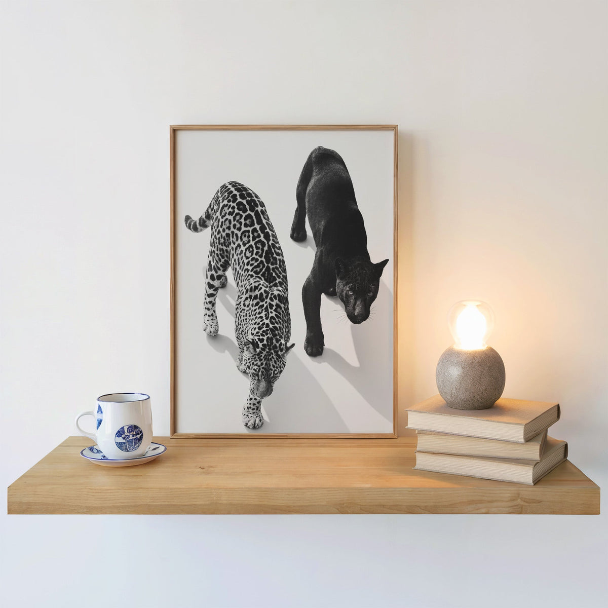 Overhead view of leopard and black panther print in an oak frame on a floating shelf beside a glowing lamp