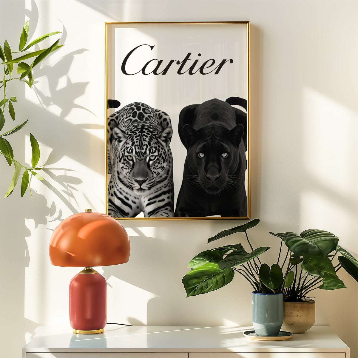 Spotted leopard and black panther pair print shown in a gold frame above a white sideboard with an orange lamp