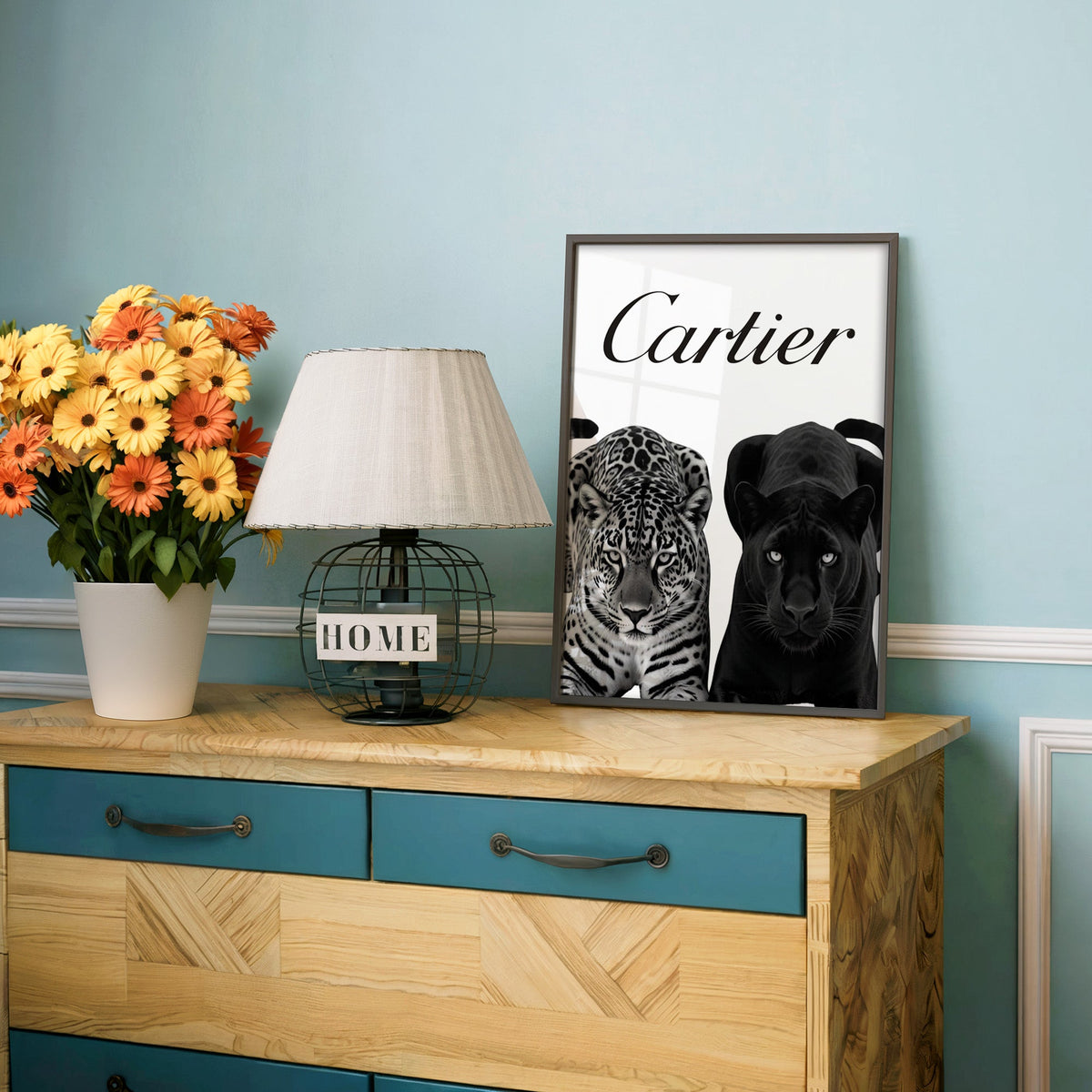 Spotted leopard and black panther pair print in a charcoal frame on a teal dresser beside orange daisies
