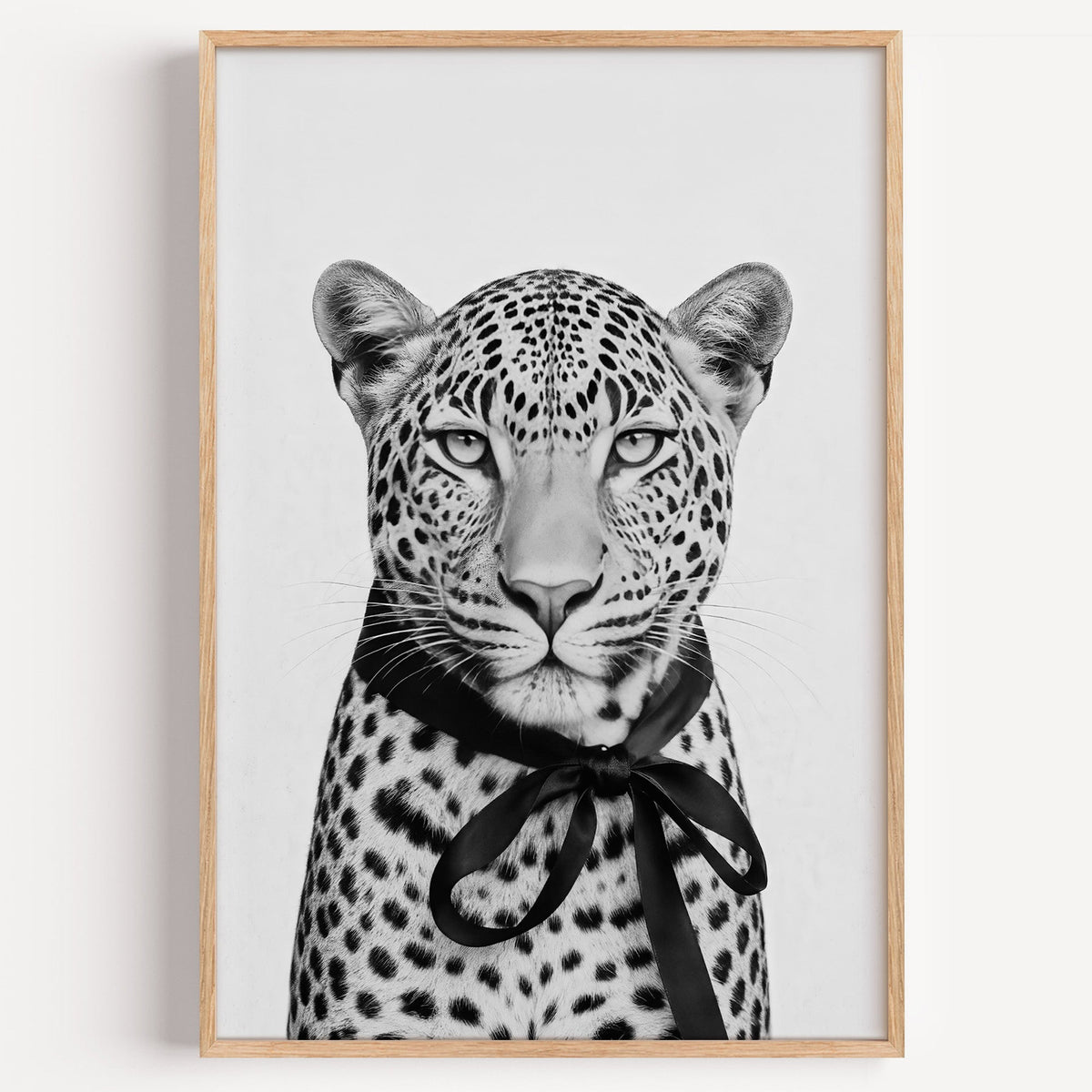 Leopard portrait with black satin bow print in a light oak frame on a plain white wall