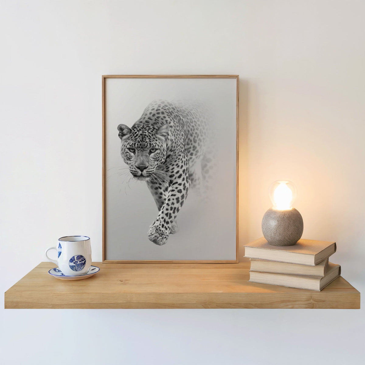 Leopard stepping out of grey mist print in an oak frame on a floating shelf beside a glowing lamp