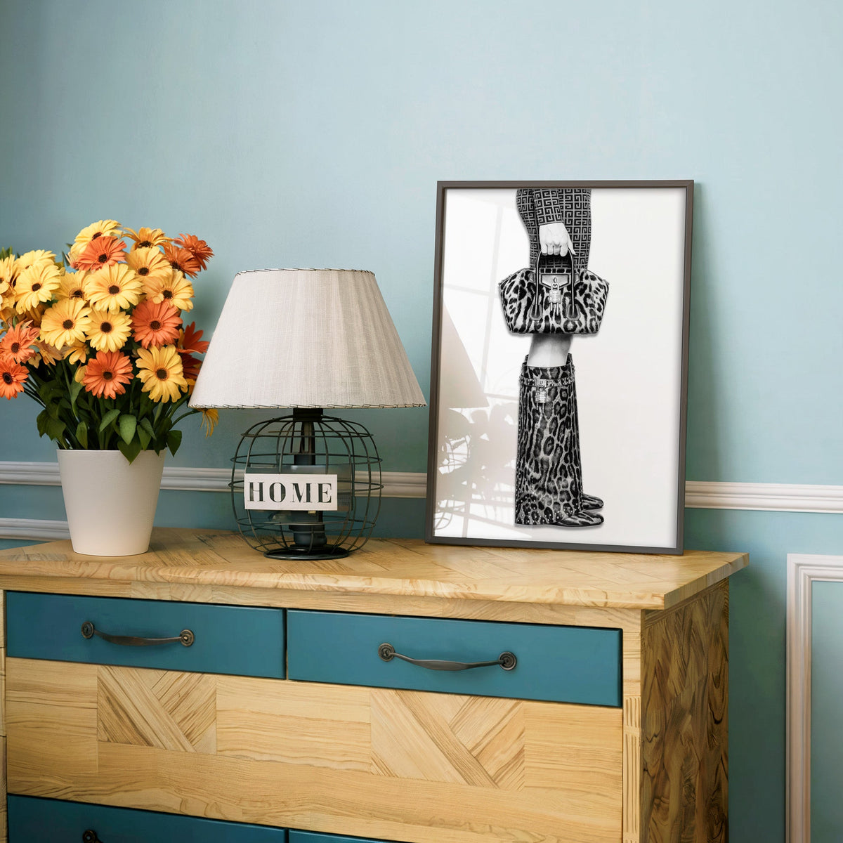 Leopard handbag and knee boots fashion photo print in a charcoal frame on a teal dresser beside orange daisies