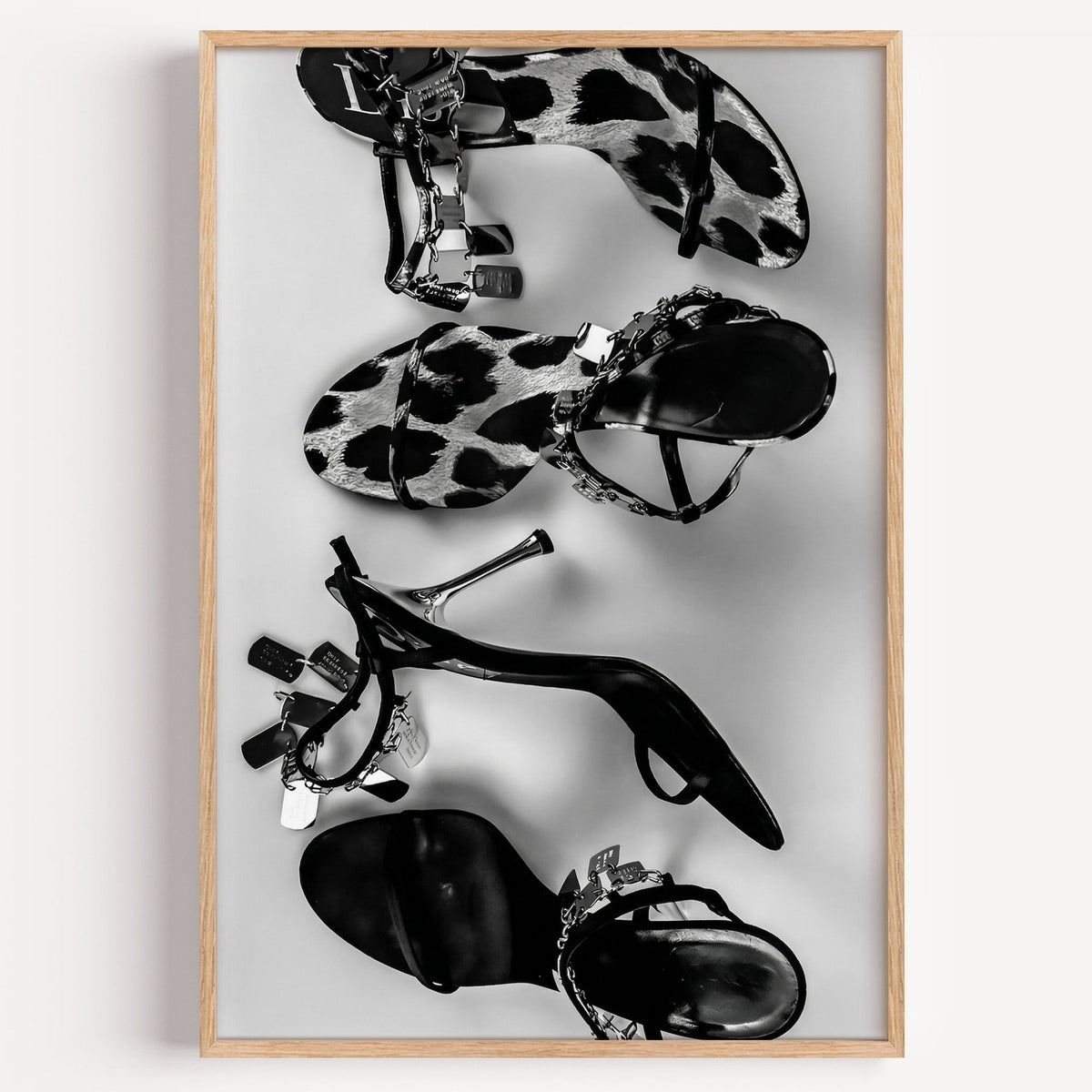 Three pairs of heeled sandals with chain straps print in a light oak frame on a plain white wall