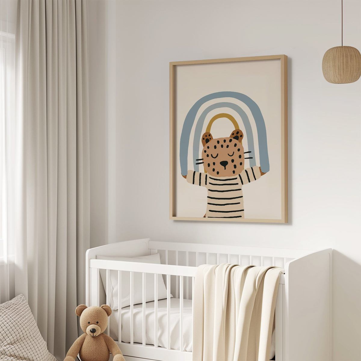 Leopard holding blue rainbow nursery print in an oak frame above a white crib with a teddy bear
