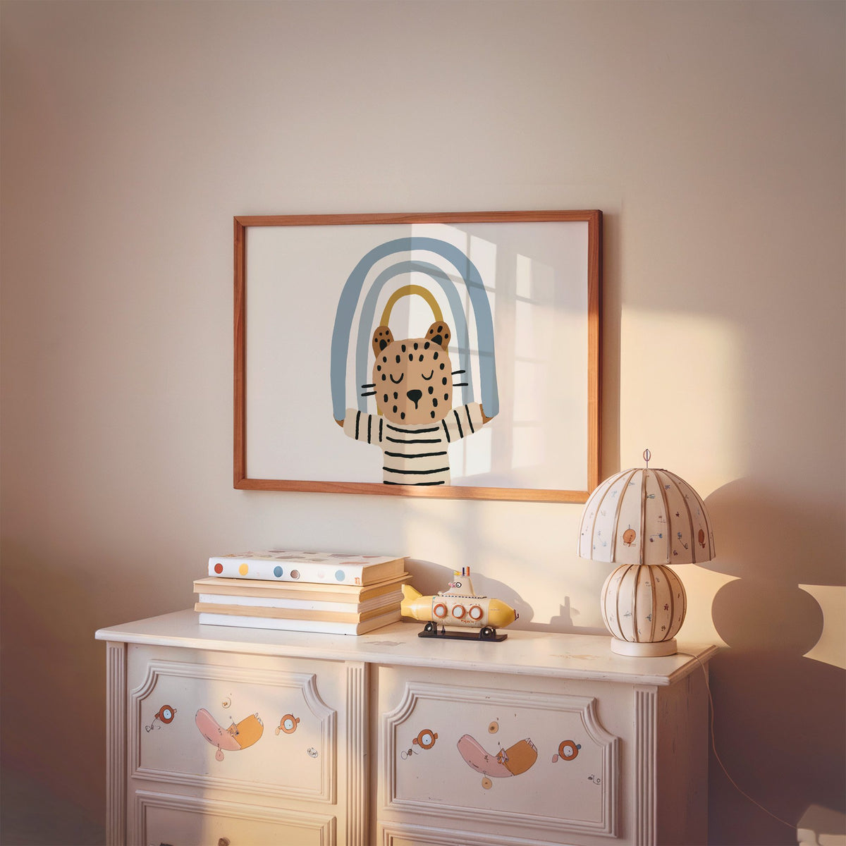 Landscape leopard holding blue rainbow nursery print in a cherry wood frame above a painted dresser and lamp