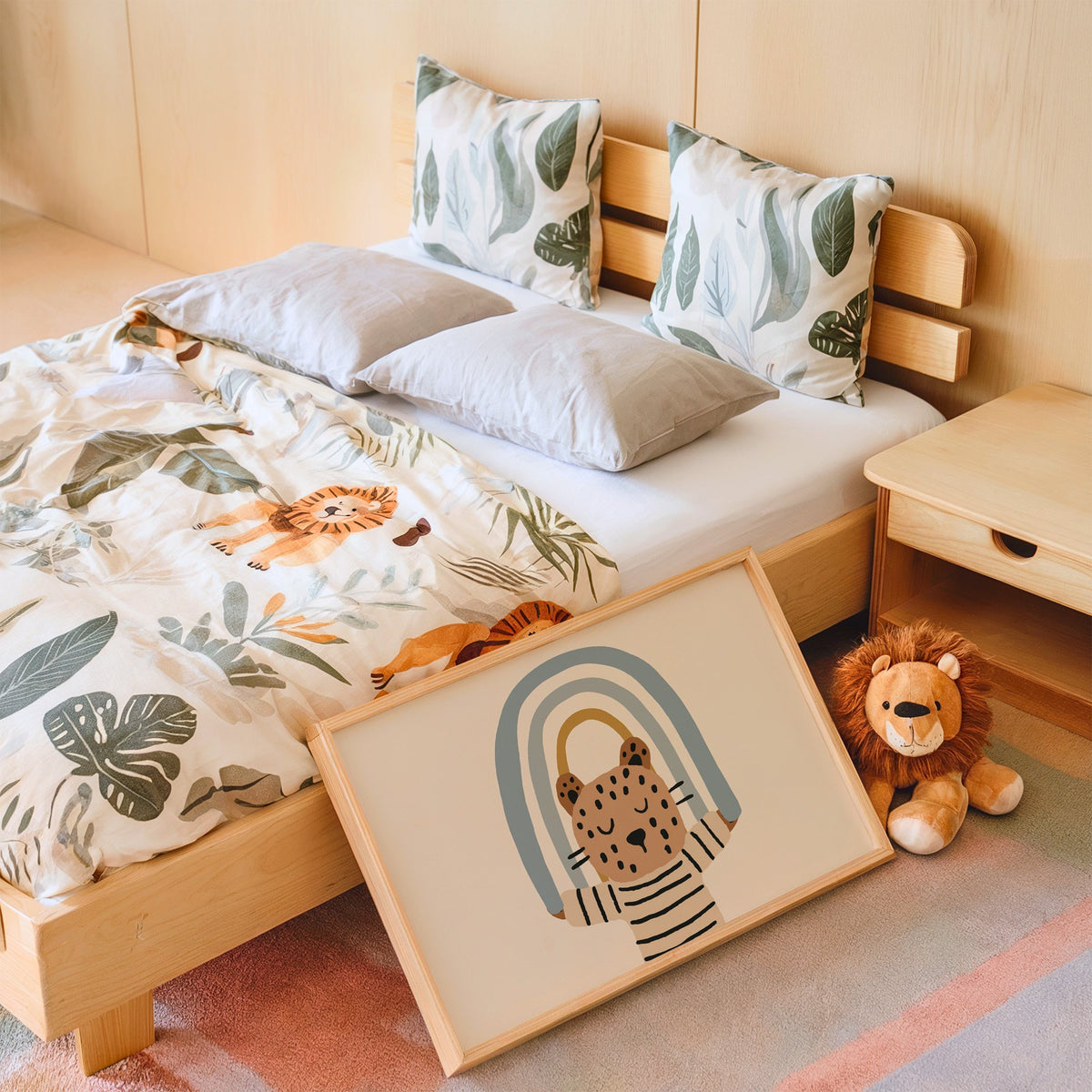 Landscape leopard holding blue rainbow nursery print in an oak frame leaning on a kids bed by a lion plush