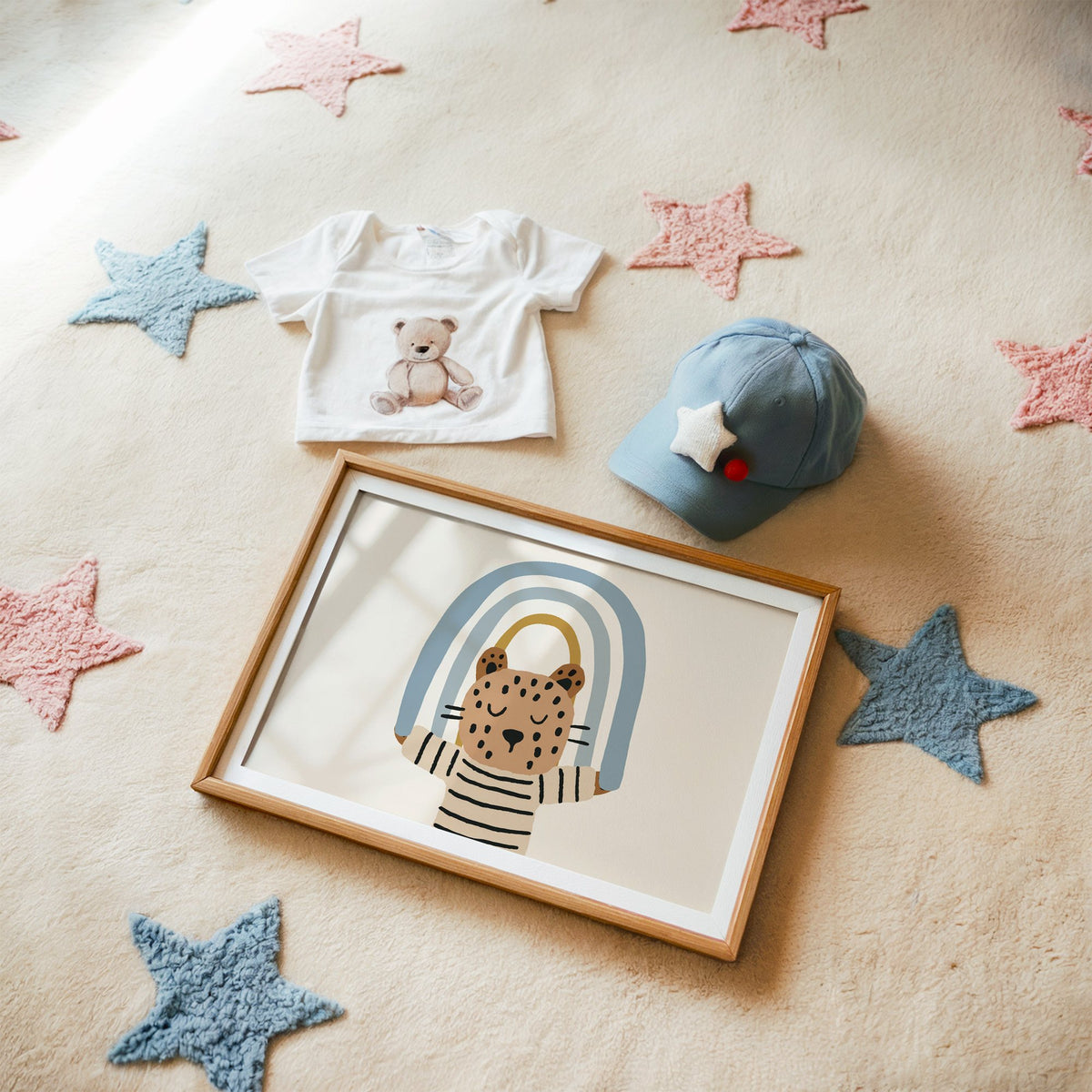 Landscape leopard holding blue rainbow nursery print in a matted oak frame on a star rug with a baby tee