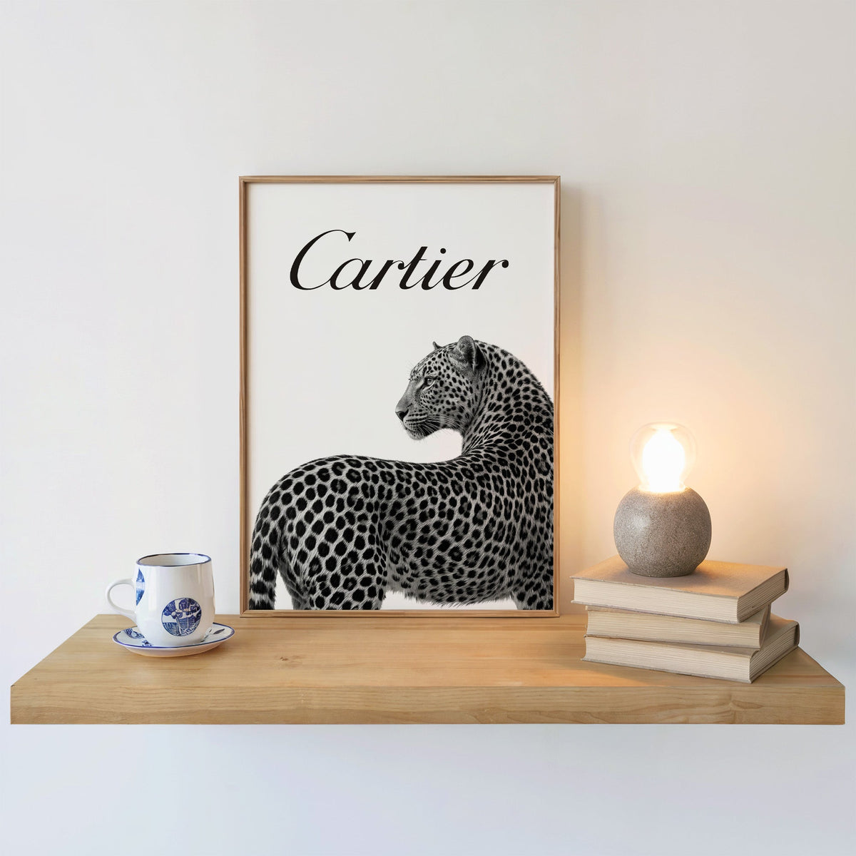 Leopard looking back below black script wordmark print in an oak frame on a floating shelf beside a glowing lamp