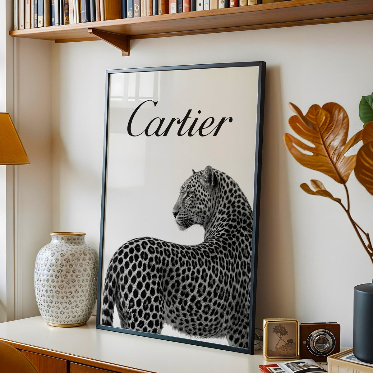 Leopard looking back below black script wordmark print in a black frame on a console under a bookshelf