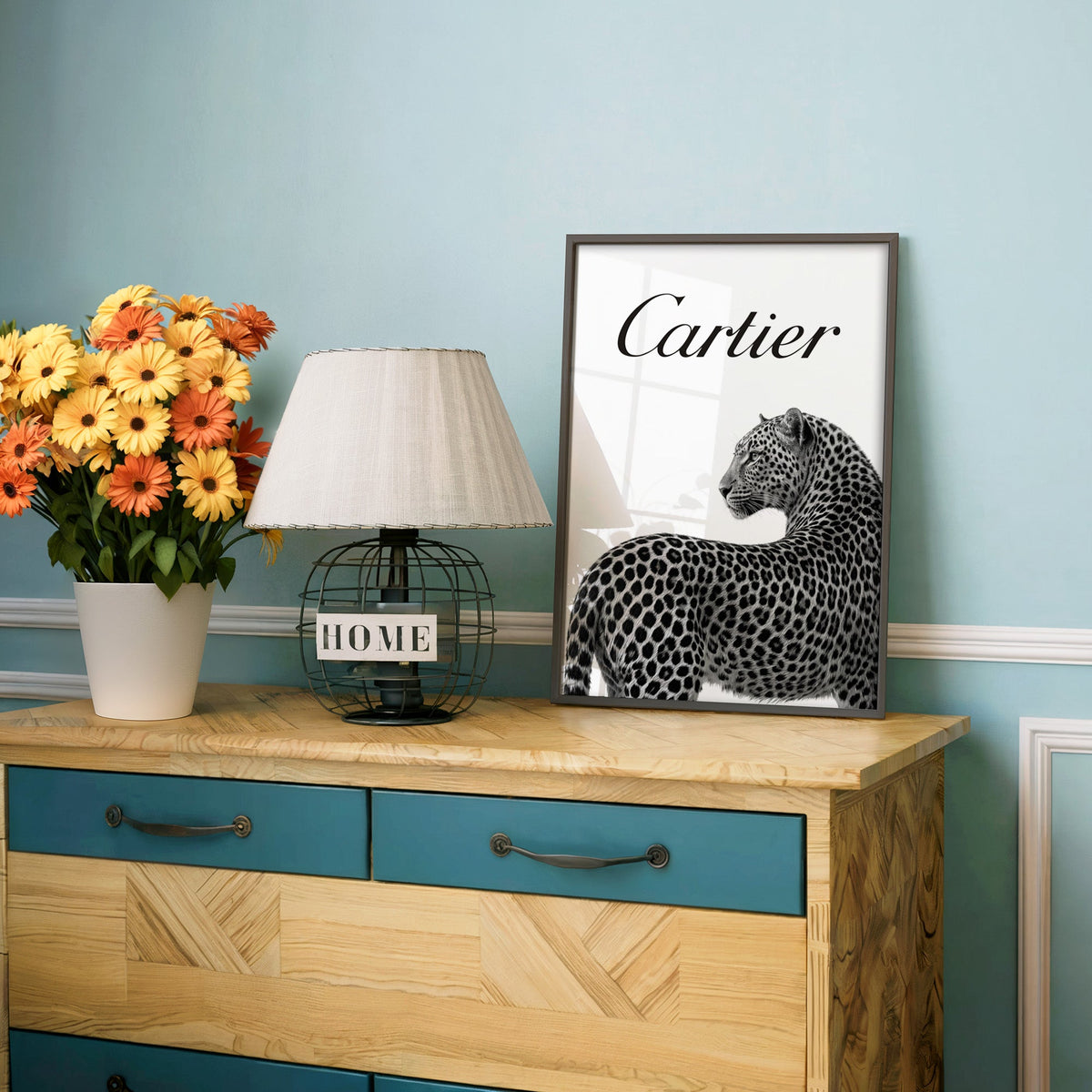 Leopard looking back below black script wordmark print in a charcoal frame on a teal dresser beside orange daisies