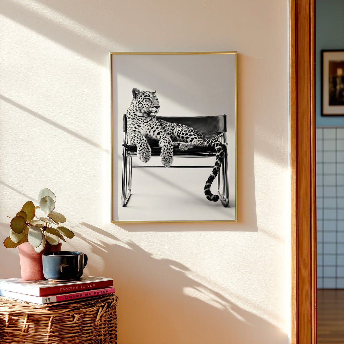 Leopard lounging on chrome tube chair print shown in a gold frame above a wicker basket and stacked books