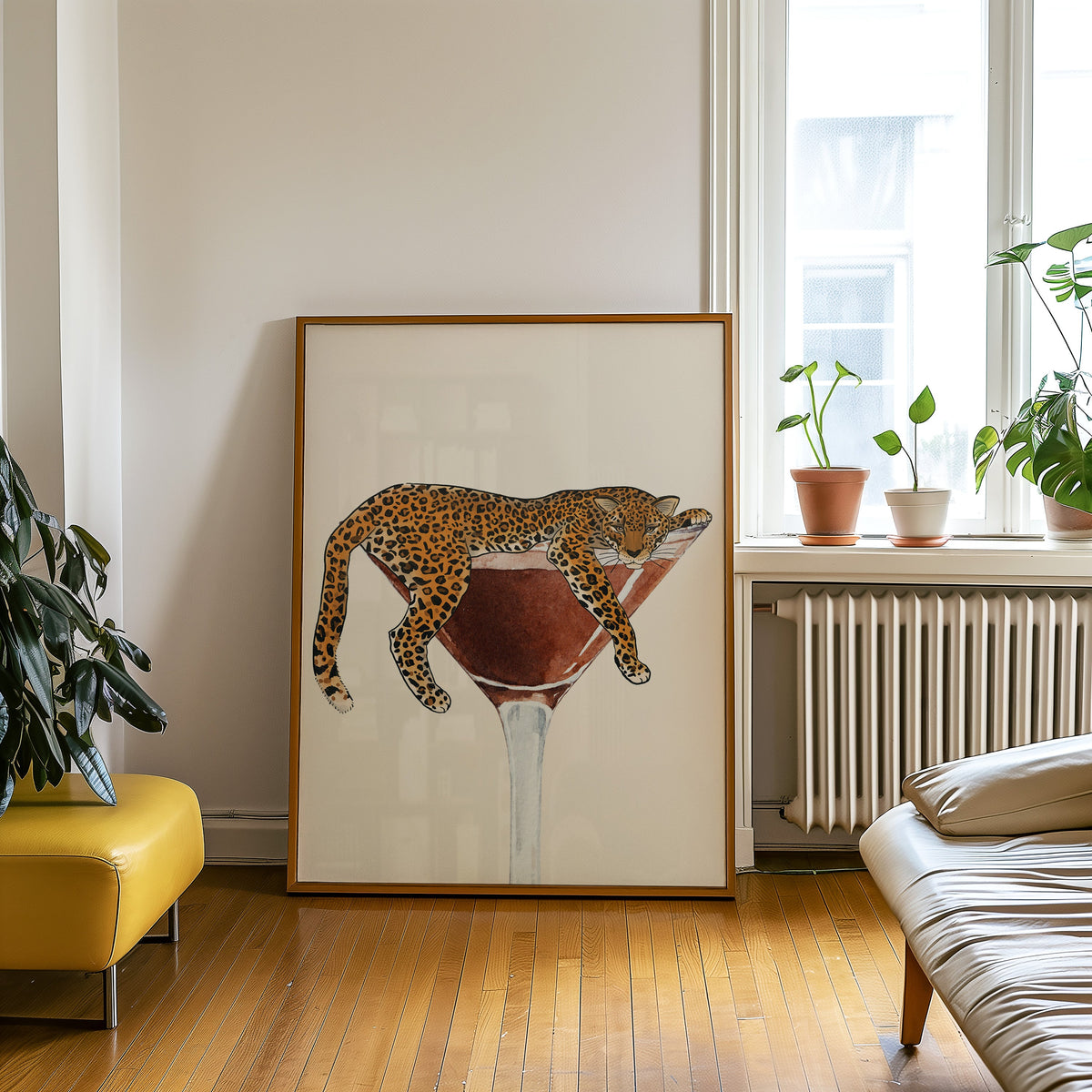 Leopard draped on a martini glass print in an oak frame leaning on a wooden floor beside a yellow leather bench