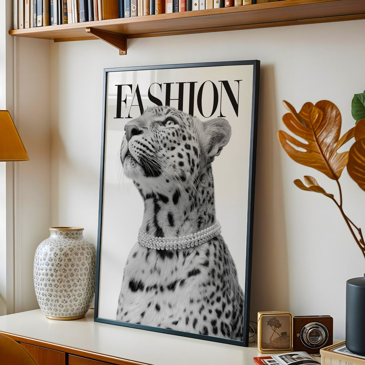 Leopard wearing pearl necklace fashion cover print in a black frame on a console under a bookshelf