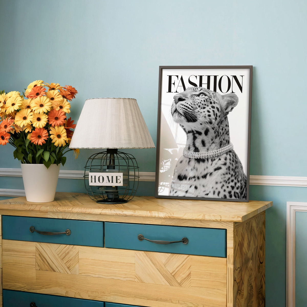Leopard wearing pearl necklace fashion cover print in a charcoal frame on a teal dresser beside orange daisies