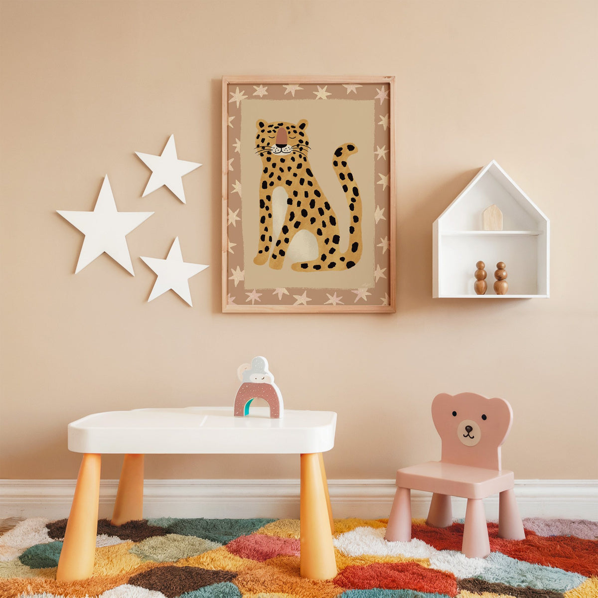 Smiling leopard with star border nursery print in an oak frame on a peach wall above a kids table with wall stars