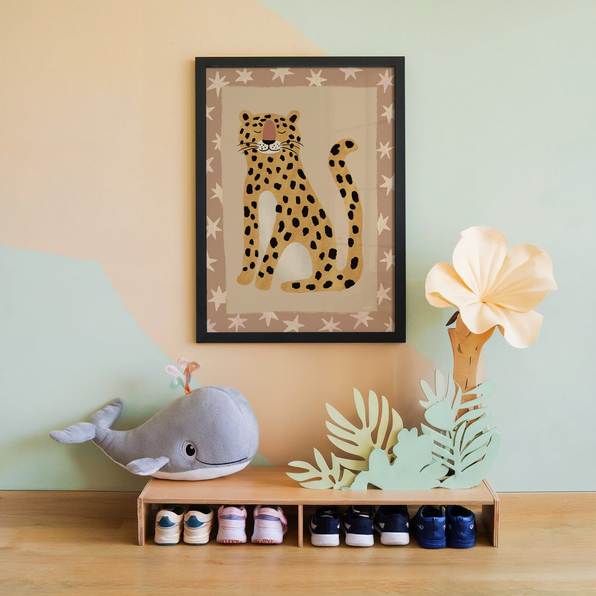 Smiling leopard with star border nursery print in a black frame on a mint and peach wall above a whale plush
