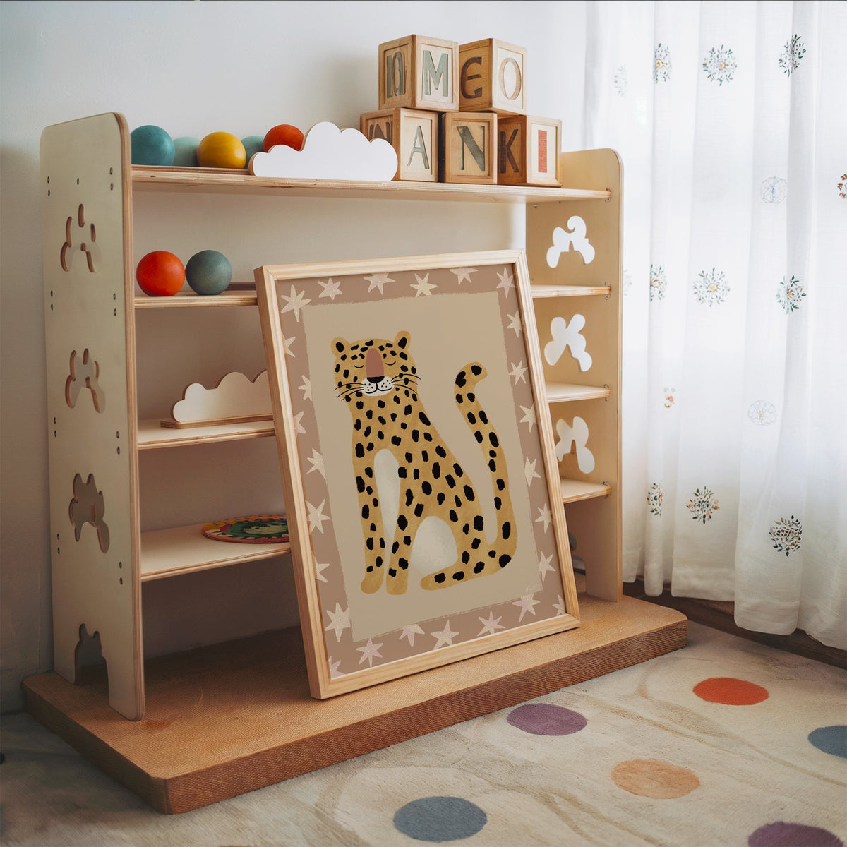 Smiling leopard with star border nursery print in an oak frame leaning on a toy shelf with wooden letter blocks